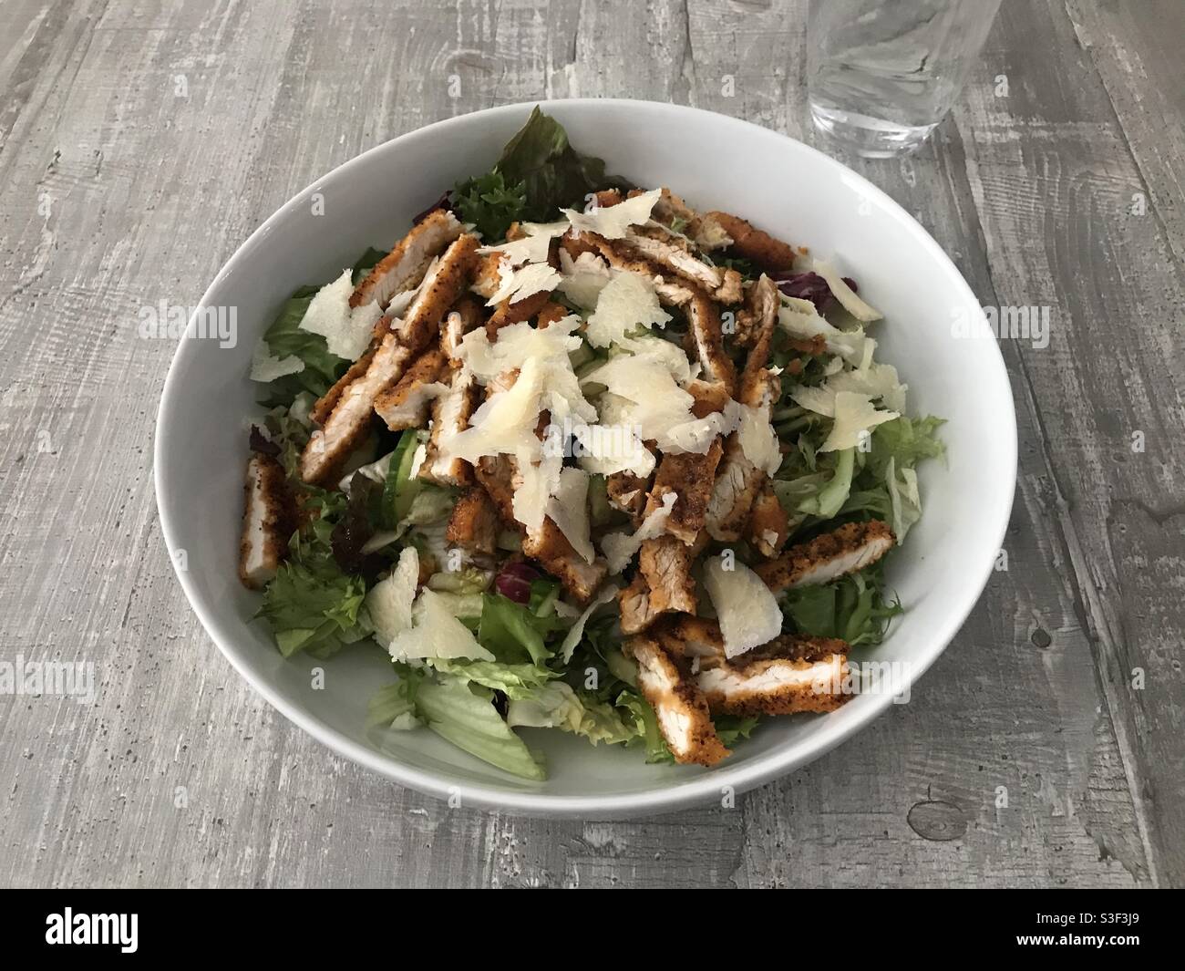 Chicken schnitzel salad topped with shavings of Parmesan cheese against a wooden background - Smartphone Captured Stock Image