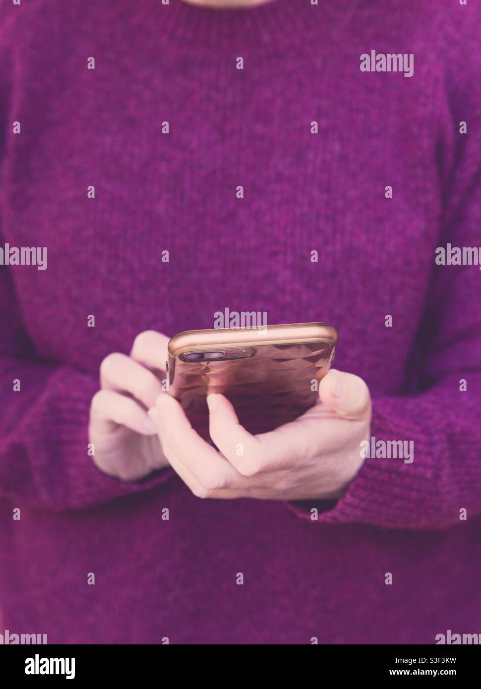 That section of a feminine girl wearing a berry coloured warm winter jumper and texting on her mobile phone or smart phone with copy space Stock Photo