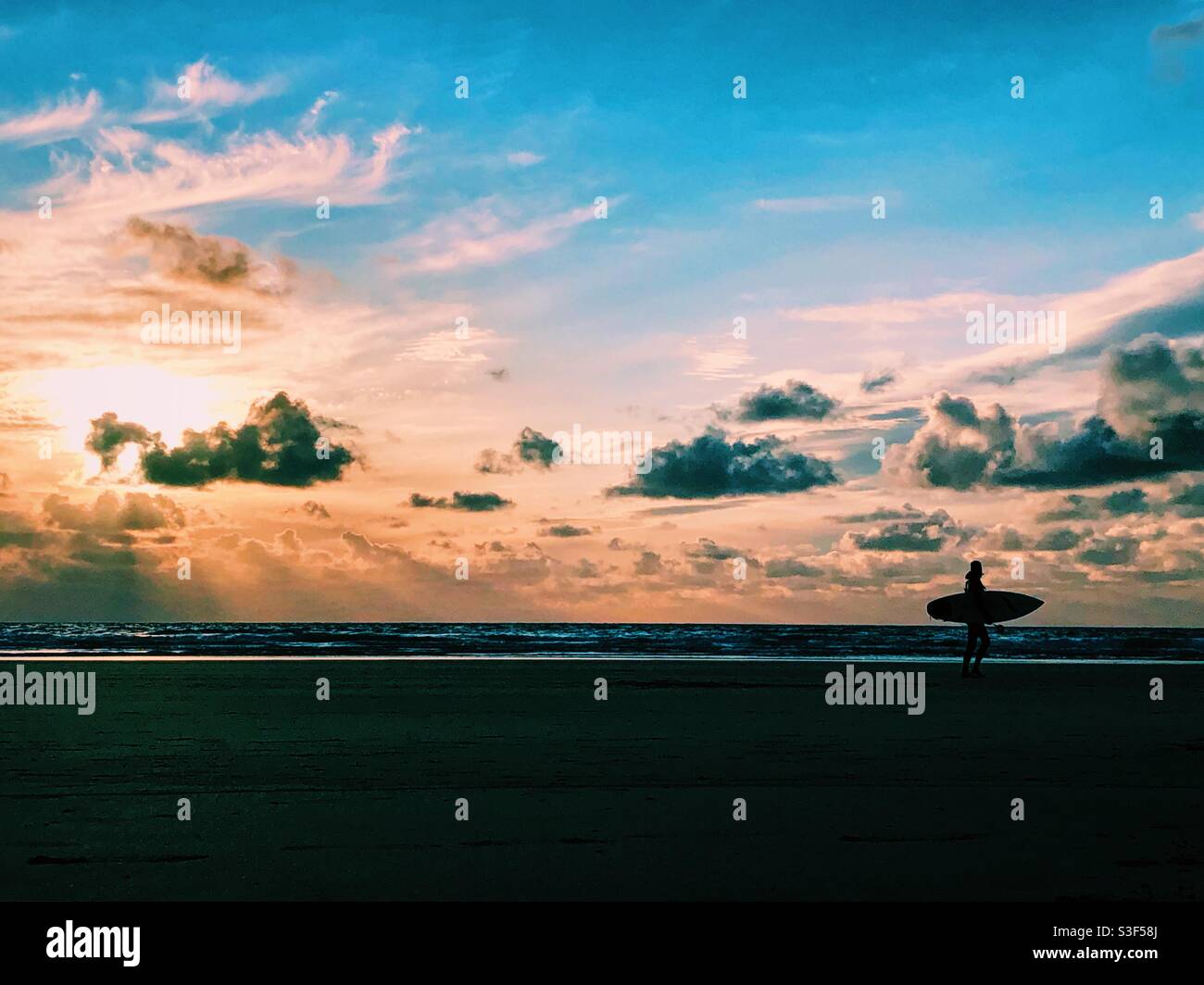 A surfer walking along the beach in Cornwall at sunset - Smartphone Captured Stock Image