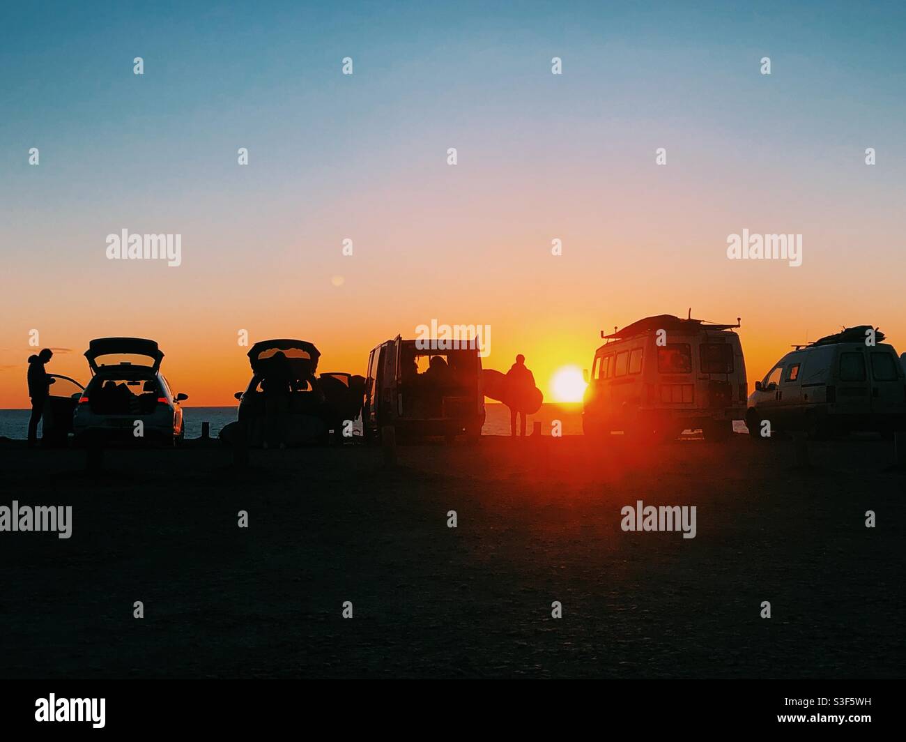 Surfers packing up their cars silhouetted by the sunset in Cornwall - Smartphone Captured Stock Image