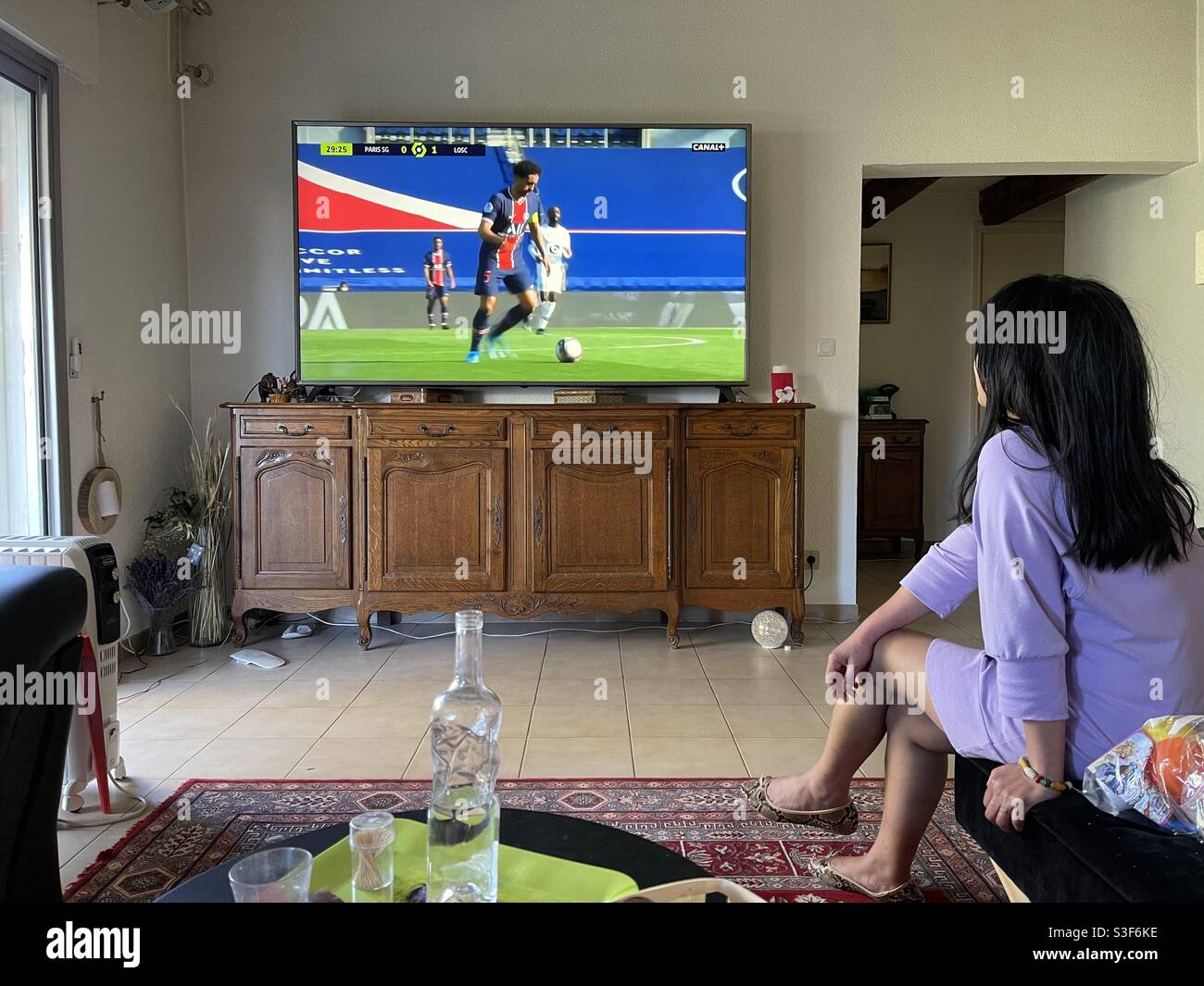 South East Asian Filipino girl watching French football on big screen television in her living room in Carnon plage near Montpellier, Occitanie, south of France Stock Photo