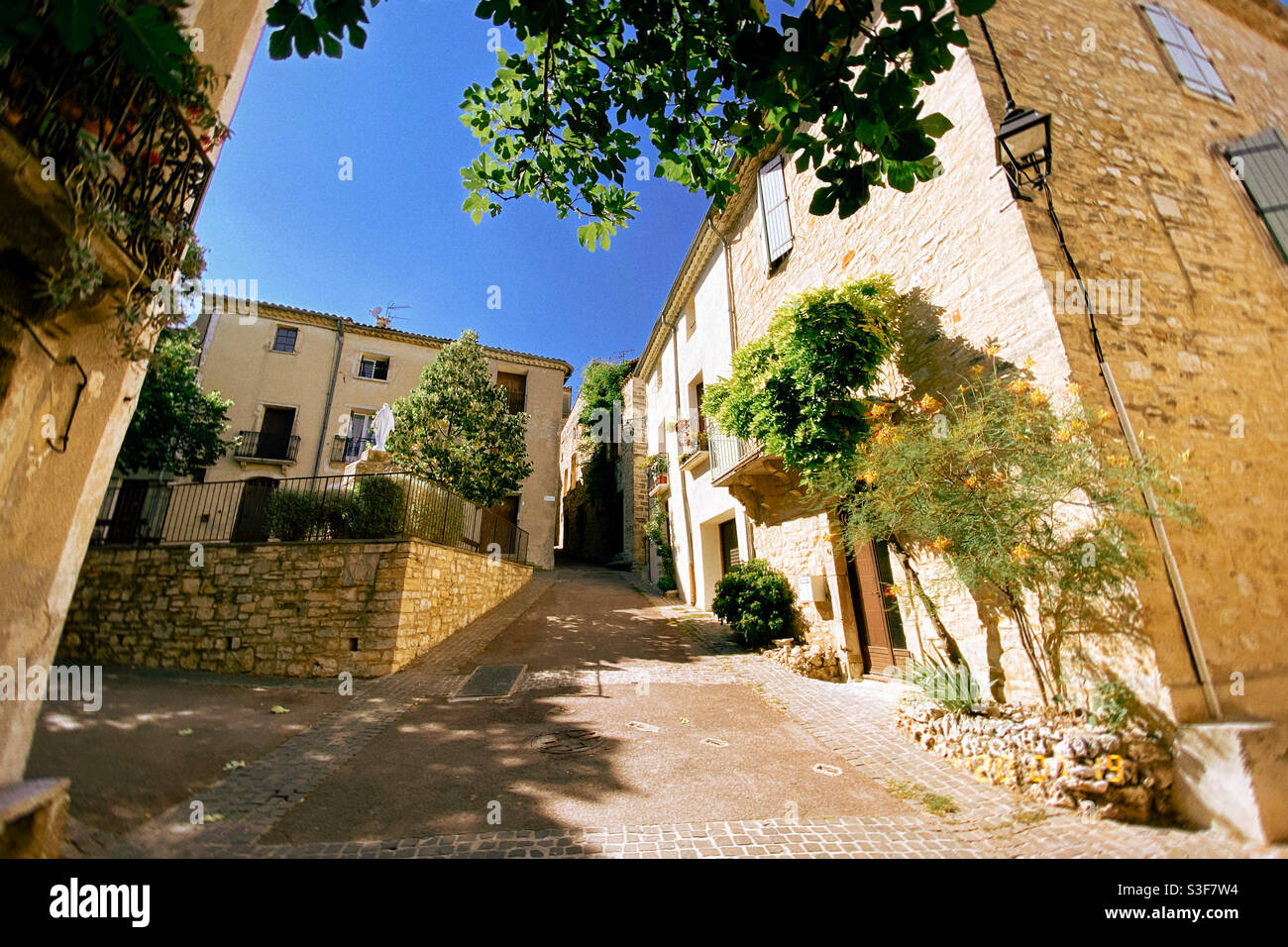 Wide paved street going uphill during the summer in a small village near Montpellier, Occitanie, south of France - Smartphone Captured Stock Image