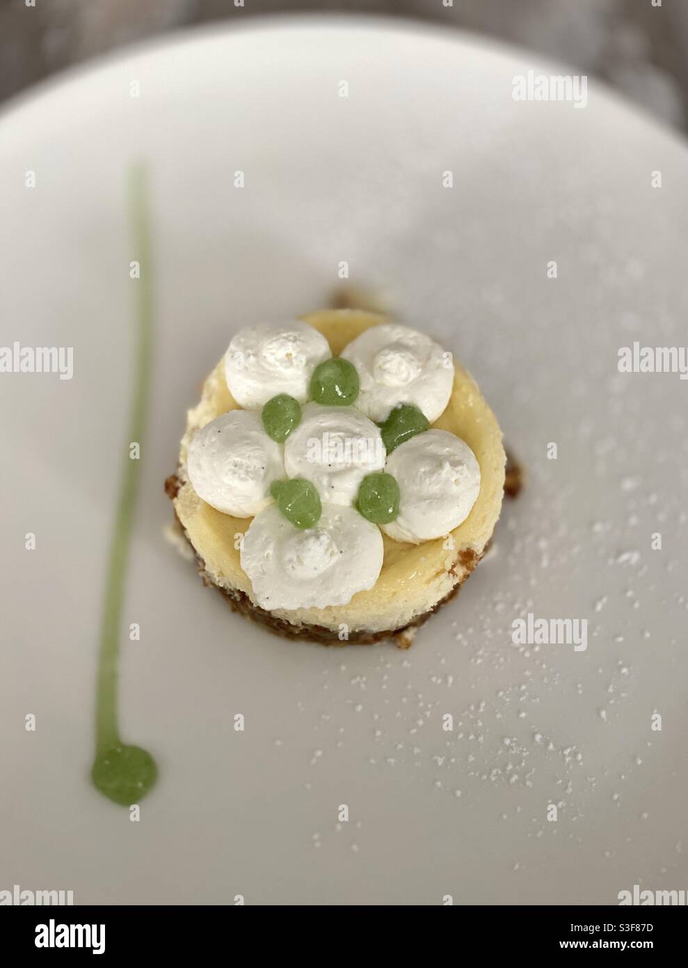 Small reconstructed lemon tart on crumble covered with homemade chantilly whipped cream and lime coulis on a white restaurant plate - Smartphone Captured Stock Image
