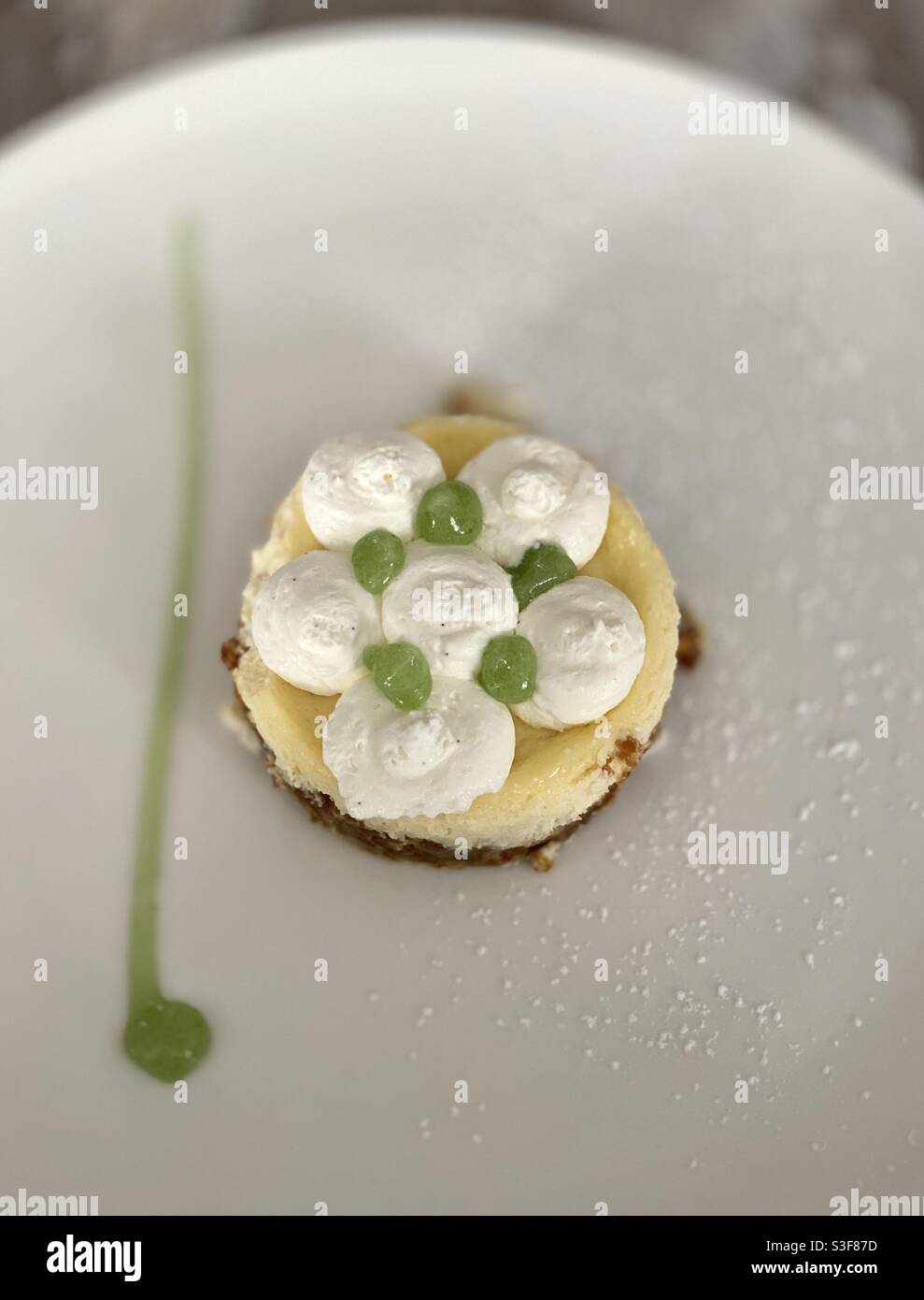 Small reconstructed lemon tart on crumble covered with homemade chantilly whipped cream and lime coulis on a white restaurant plate Stock Photo