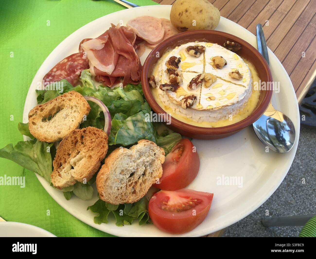 Salad with croutons, cold cuts and a fried Camembert cheese with nuts on a restaurant plate in small French village Valergues near Montpellier, Occitanie, south of France Stock Photo