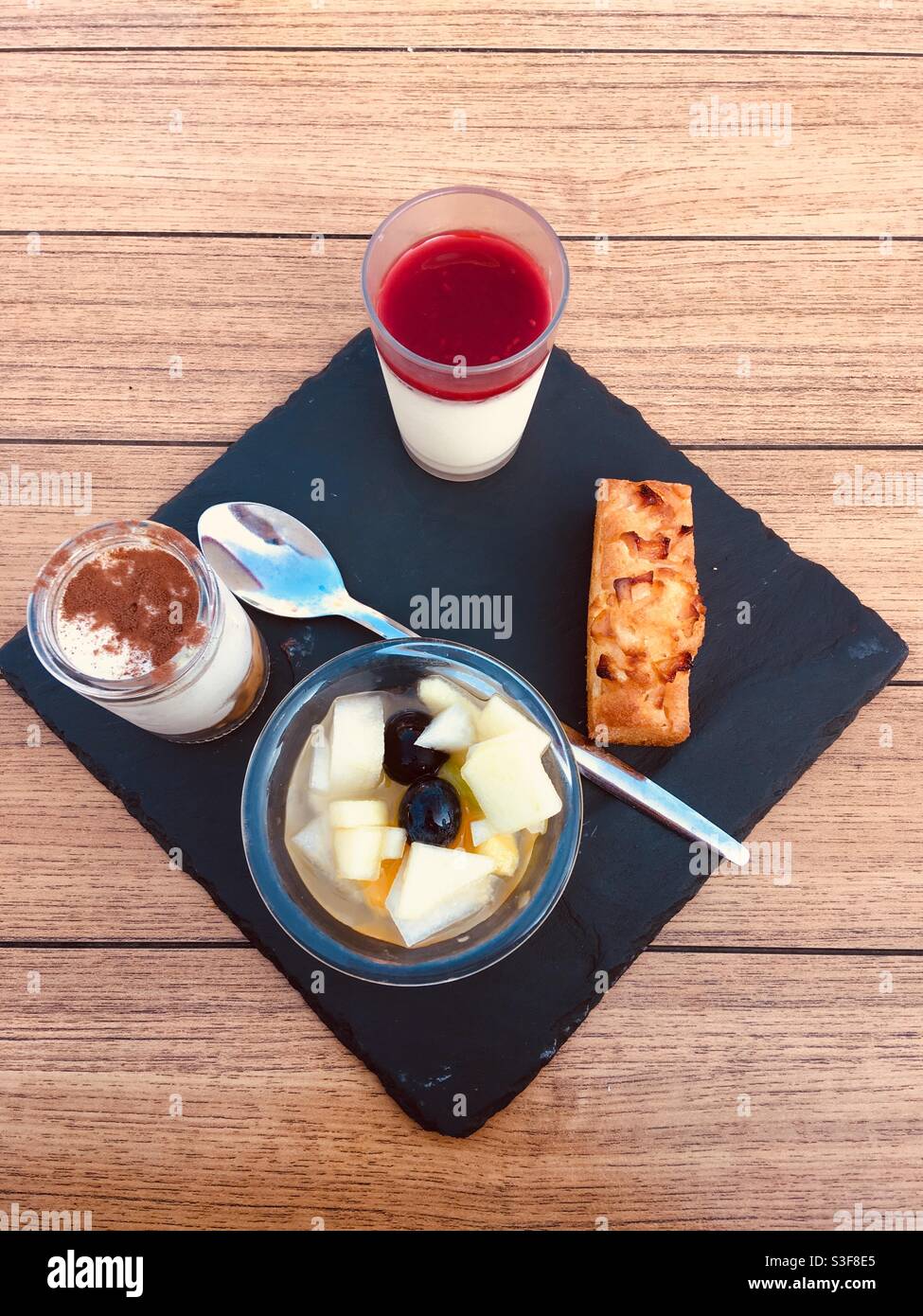 Selection of four desserts square stone plate dish in a French restaurant : Panna Cotta with red fruit coulis, reconstructed whipped cream Tiramisu, fruit salad in syrup and a slice of apple pie - Smartphone Captured Stock Image