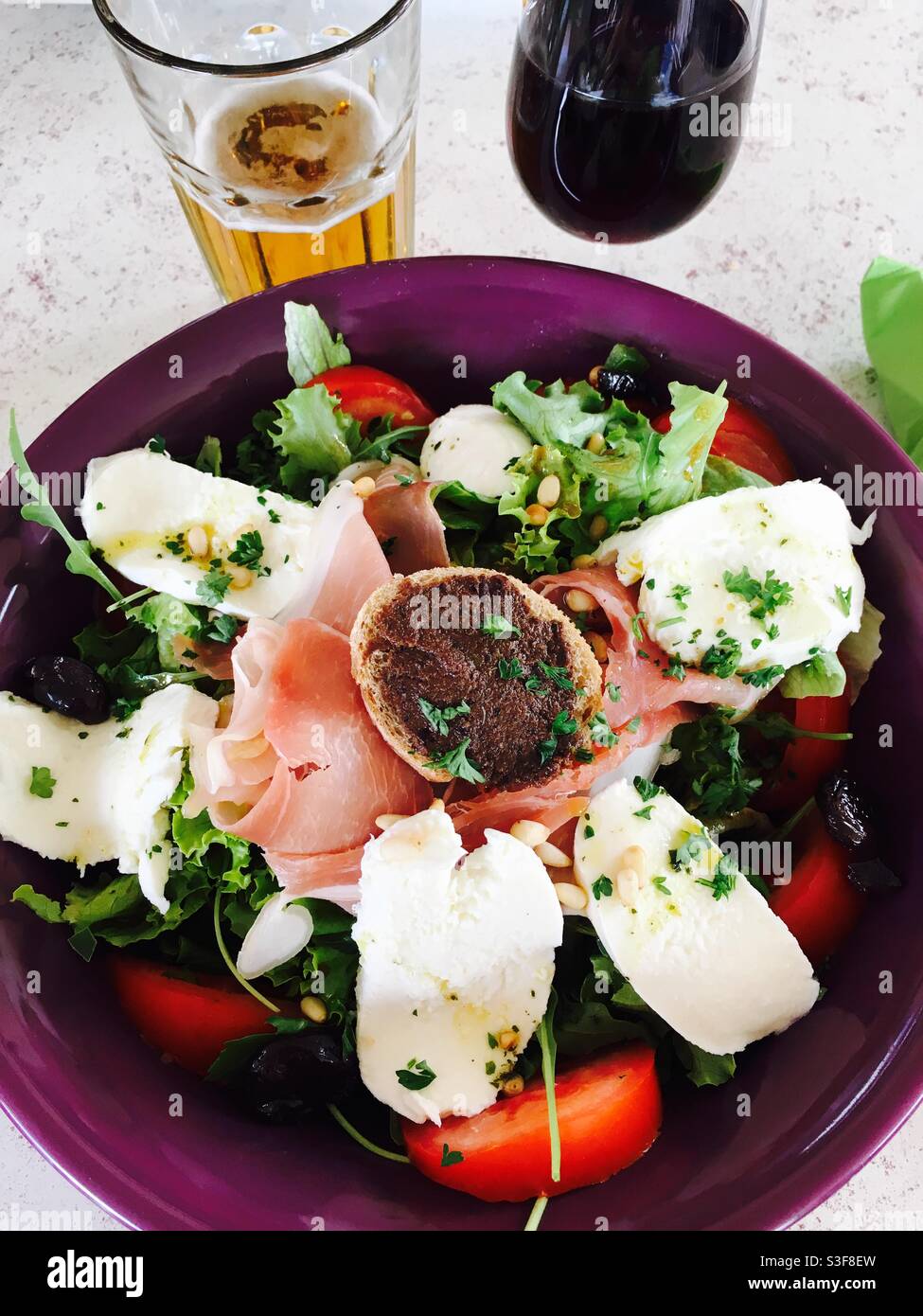 Hot goat cheese salad with a olive paste marmelade on toasted bread with tomatoes with a glass of beer and red wine - Smartphone Captured Stock Image