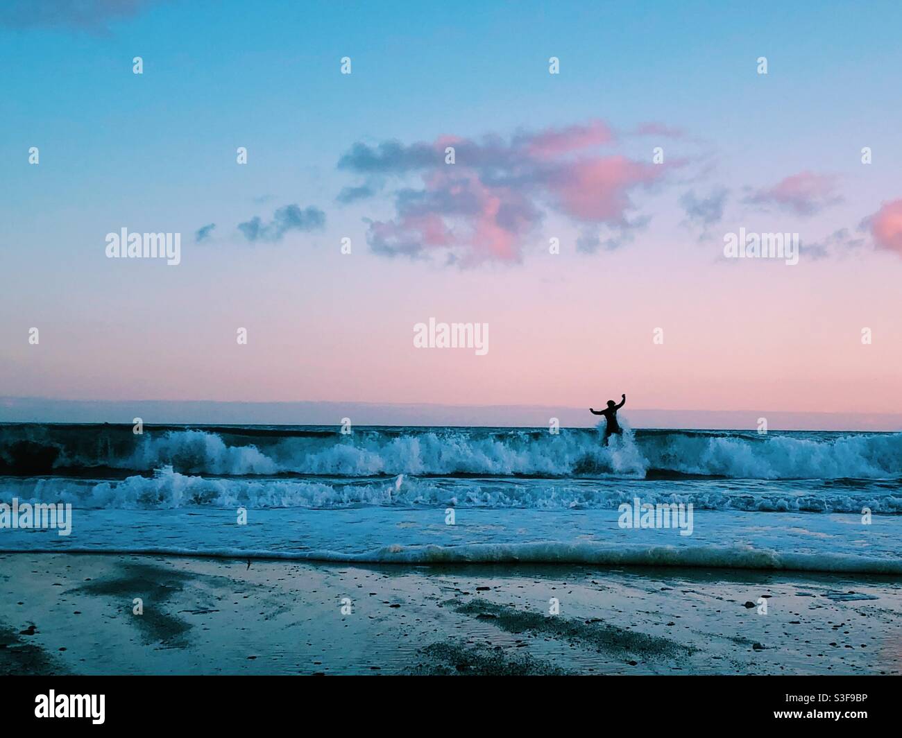 A surfer silhouetted by the sunset at praa sands beach in Cornwall - Smartphone Captured Stock Image