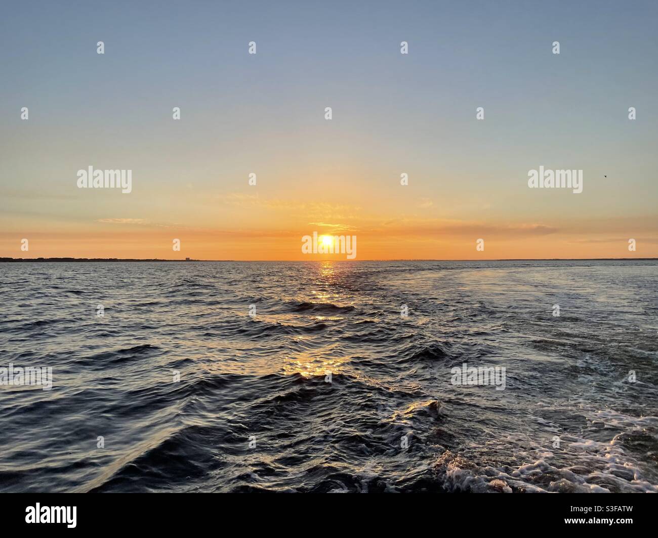 Golden sunset skies with boat wake waves over the Gulf of Mexico water ...