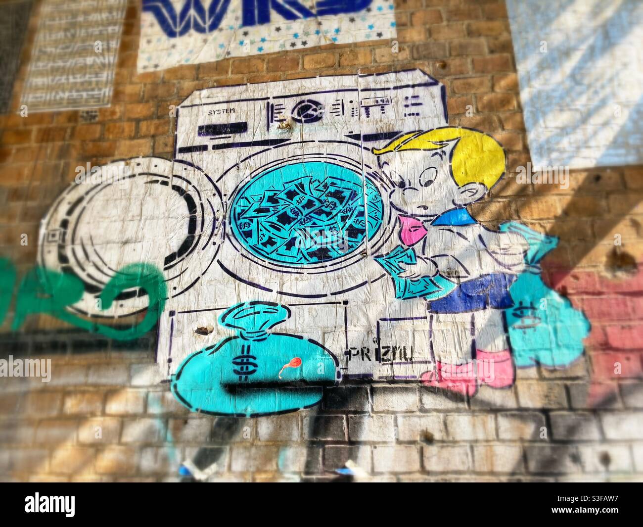 A cut-out Street Art By Prizmu of a blonde boy laundering Money in a washing machine, Berlin, Germany - Smartphone Captured Stock Image