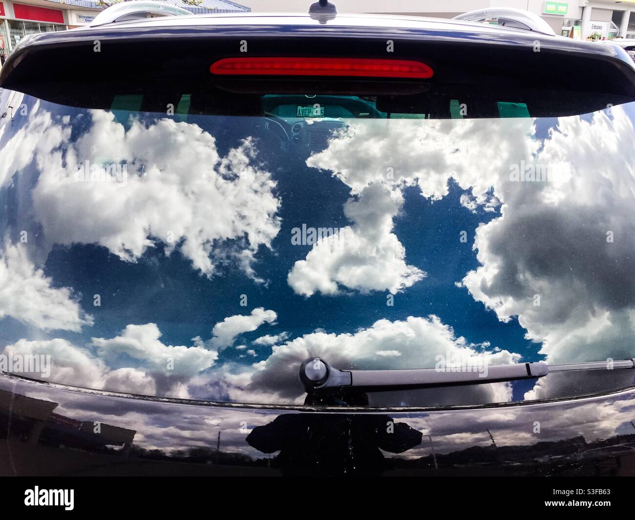 Summer time. Cumulus clouds reflected in the rear window of an SUV. Conceptual: invitation, to fly, to Dream, travel, take off, wanderlust, go - Smartphone Captured Stock Image