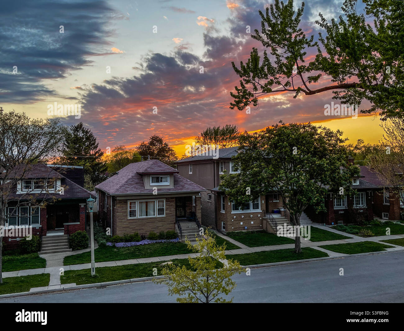 Clouds over bungalows in Oak Park, Illinois neighborhood illuminated by setting sun. Stock Photo