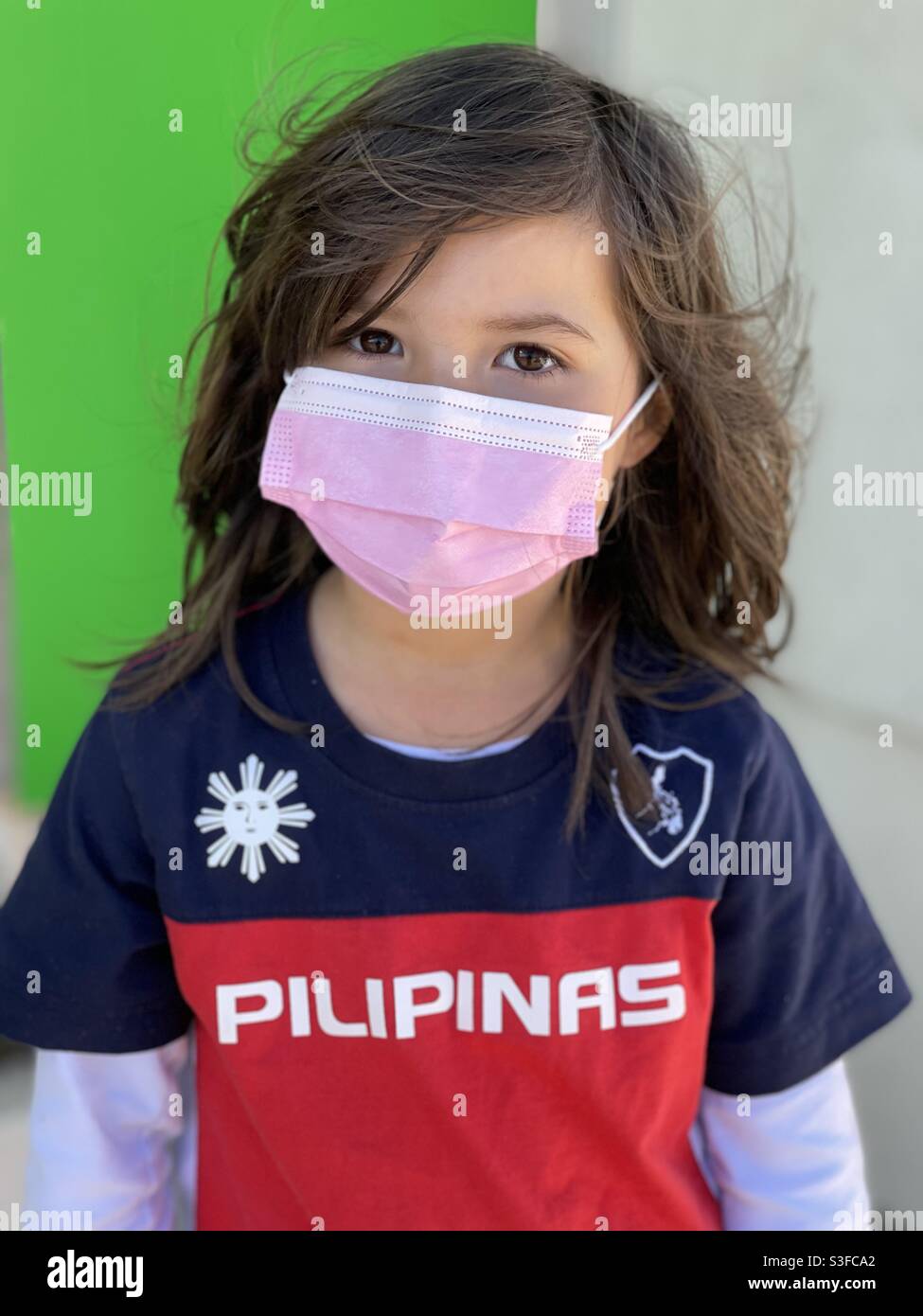 Mixed Asian filipino little girl with long brown hair wearing a pink mask and a blue, red and white Pilipinas t-shirt Stock Photo