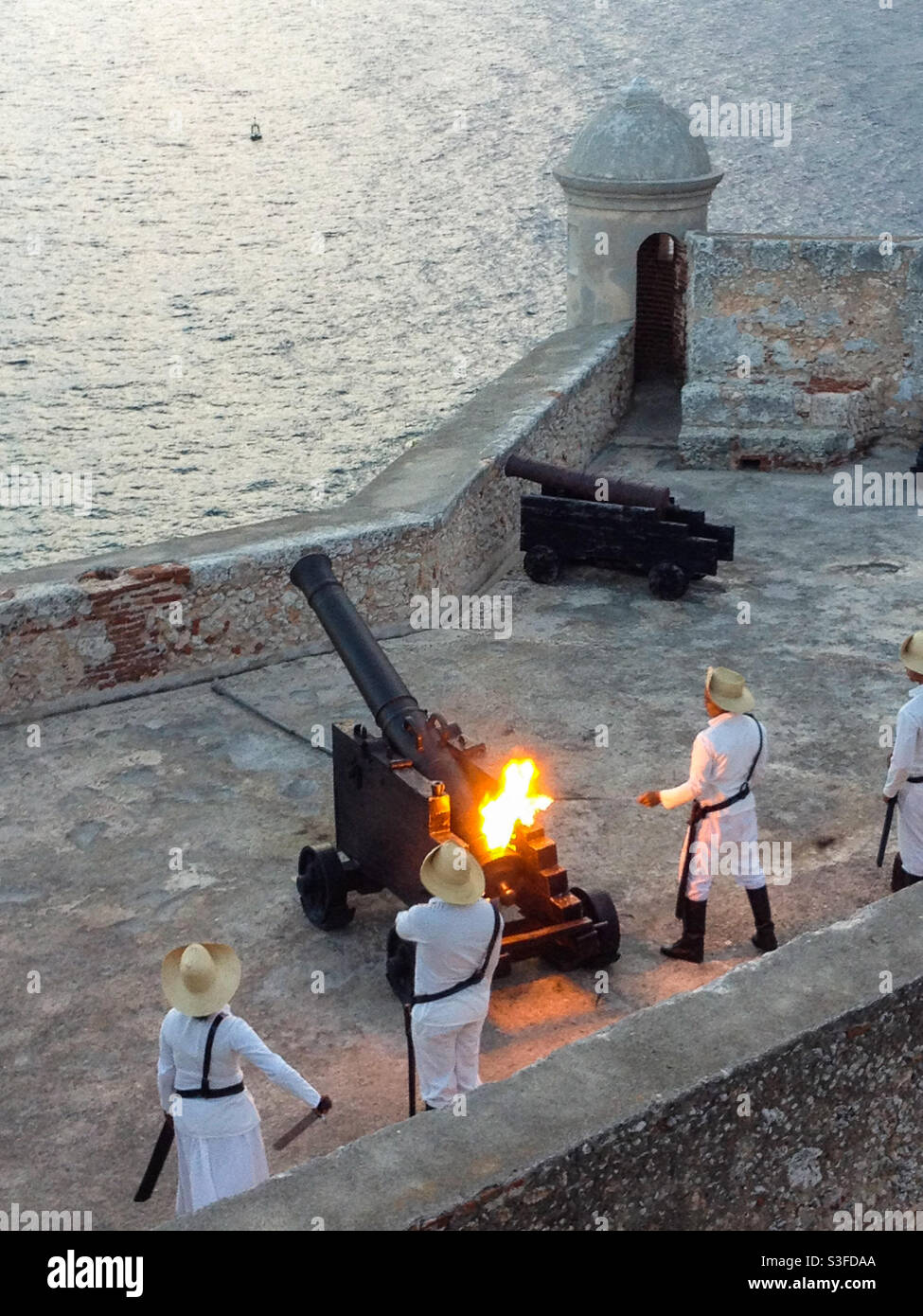 Cadets in uniform firing canon on castle wall at Castillo de San Pedro de la Ricardo or Morro Castle, Santiago de Cuba, Cuba - Smartphone Captured Stock Image