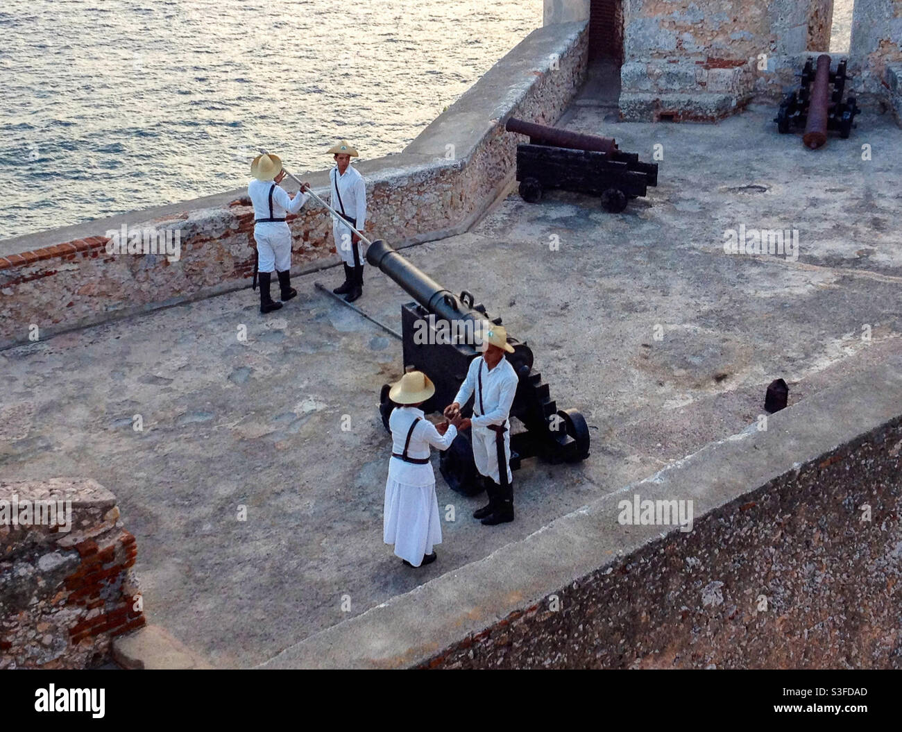Cadets in uniform prepare to fire cannon on castle rampart to entertain tourists at Castillo de San Pedro de la Roca or Morro fortified castle, Santiago de Cuba, Cuba - Smartphone Captured Stock Image