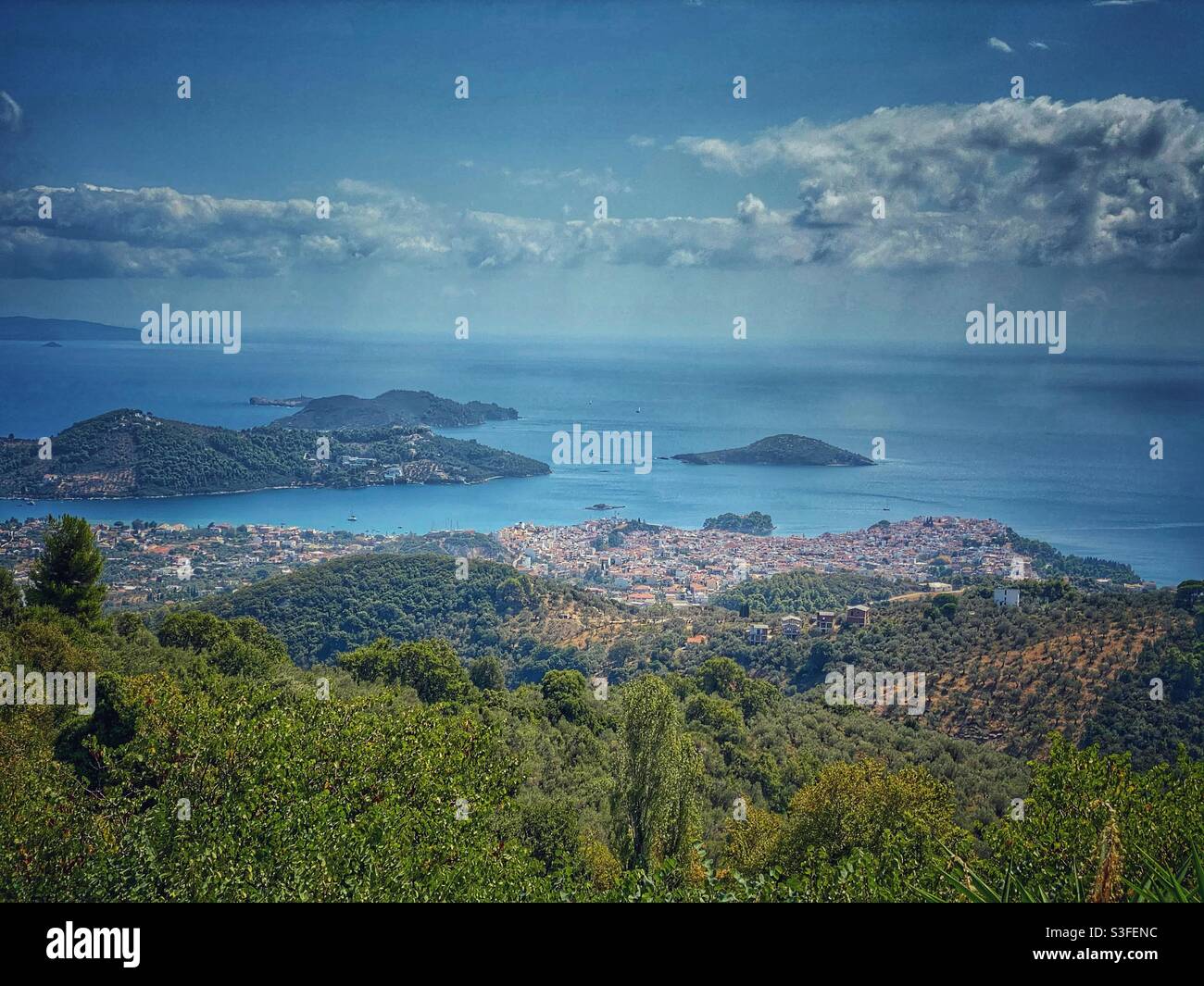 Seascape view at Skiathos island and town with green trees in the foreground, Greece. - Smartphone Captured Stock Image