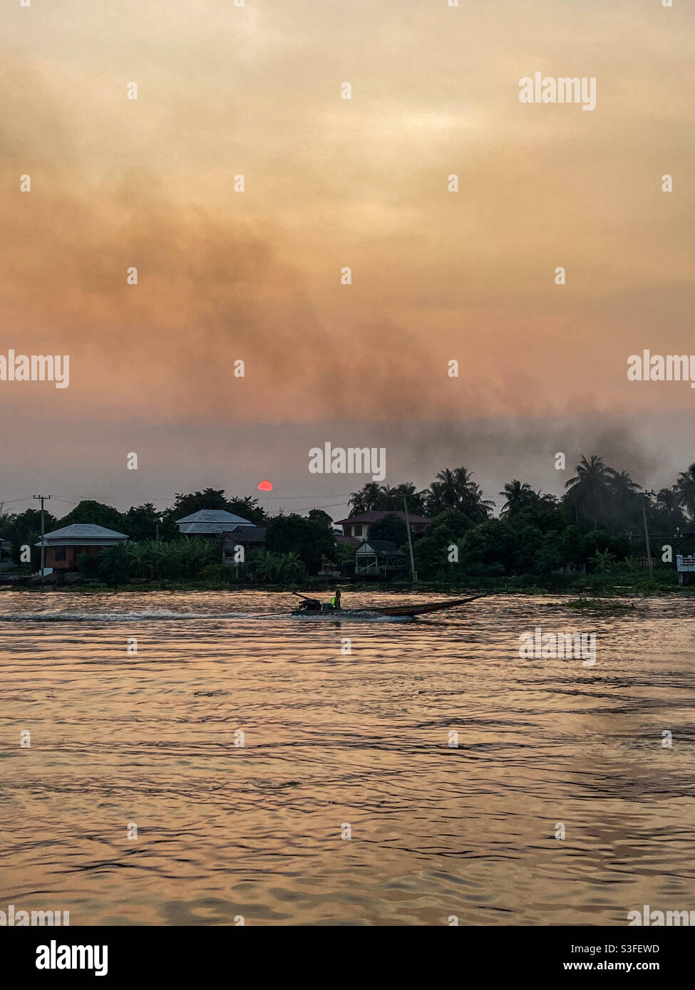 Smoke pollution coming from a boat on a river in Southeast Asia at sunset. Stock Photo