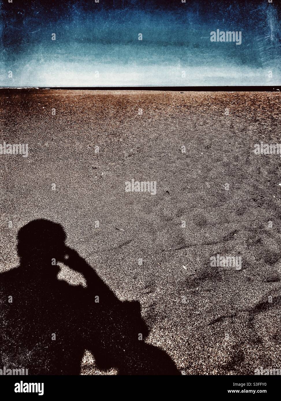 Moody image of shadow of a man thinking on the beach - Smartphone Captured Stock Image