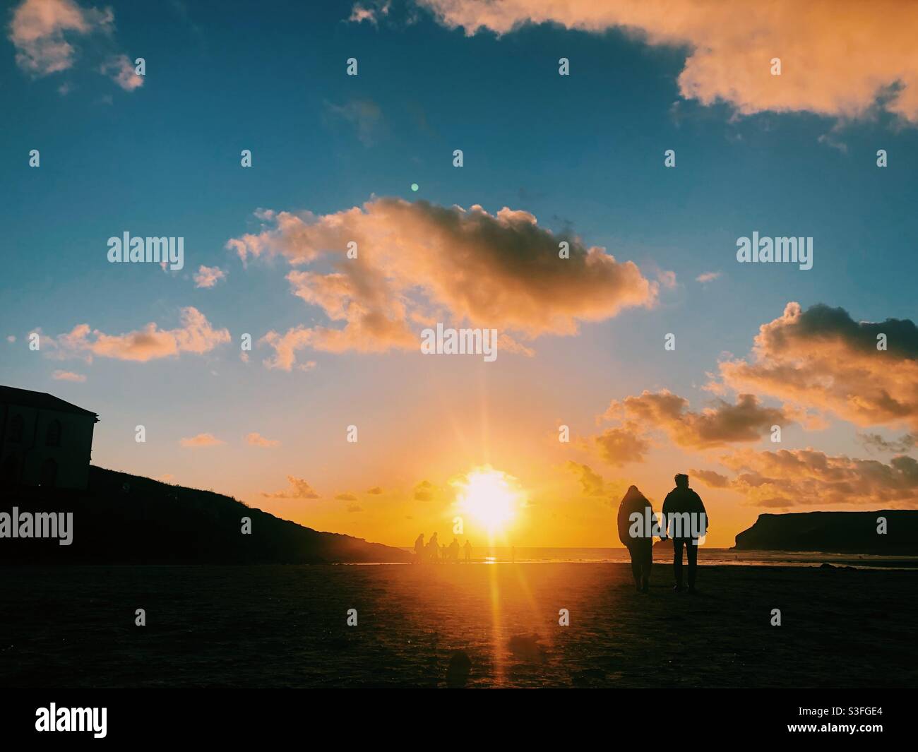 A couple walk towards the sunset holding hands on a beach in Cornwall - Smartphone Captured Stock Image