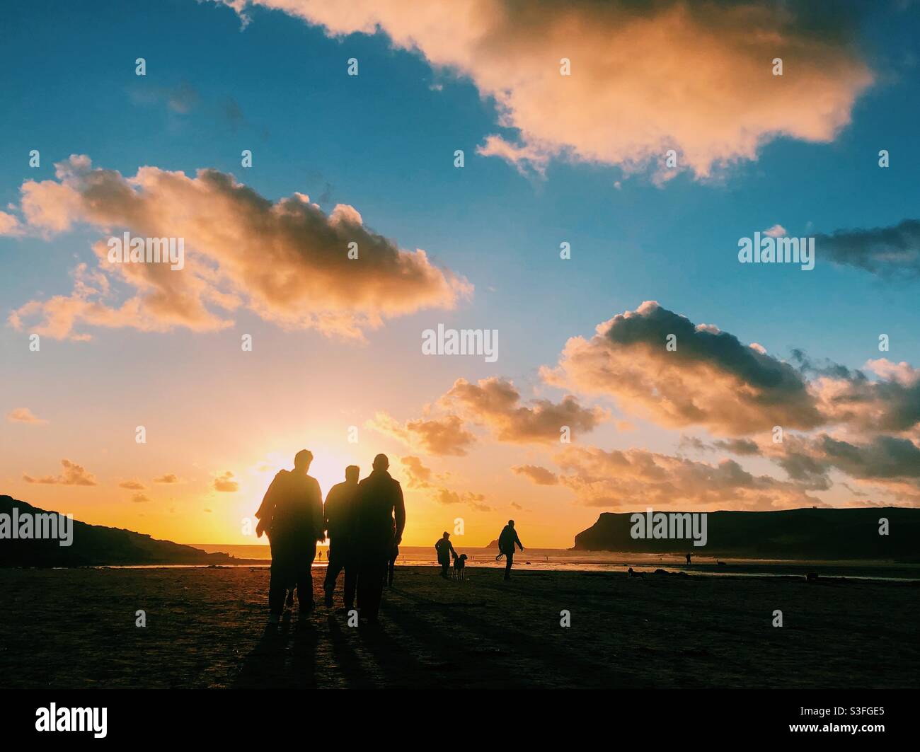 People silhouetted in front of a sunset on a beach in Cornwall - Smartphone Captured Stock Image