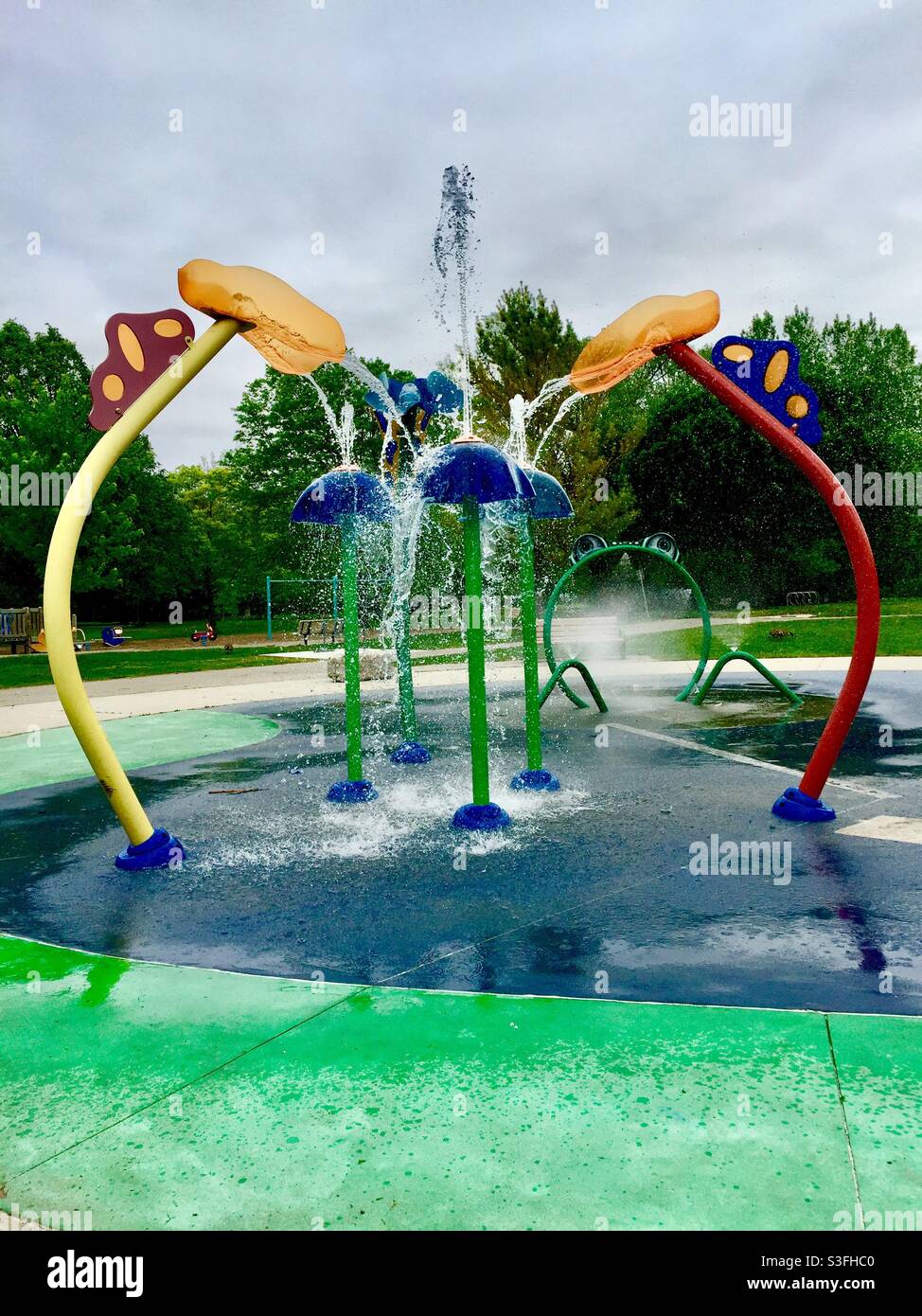 Contemporary splash pad and swings in green surroundings, Ontario, Canada. Popular spot for cooling off and fun in spring, summer, and early fall. Pretty sight in winter, too. - Smartphone Captured Stock Image