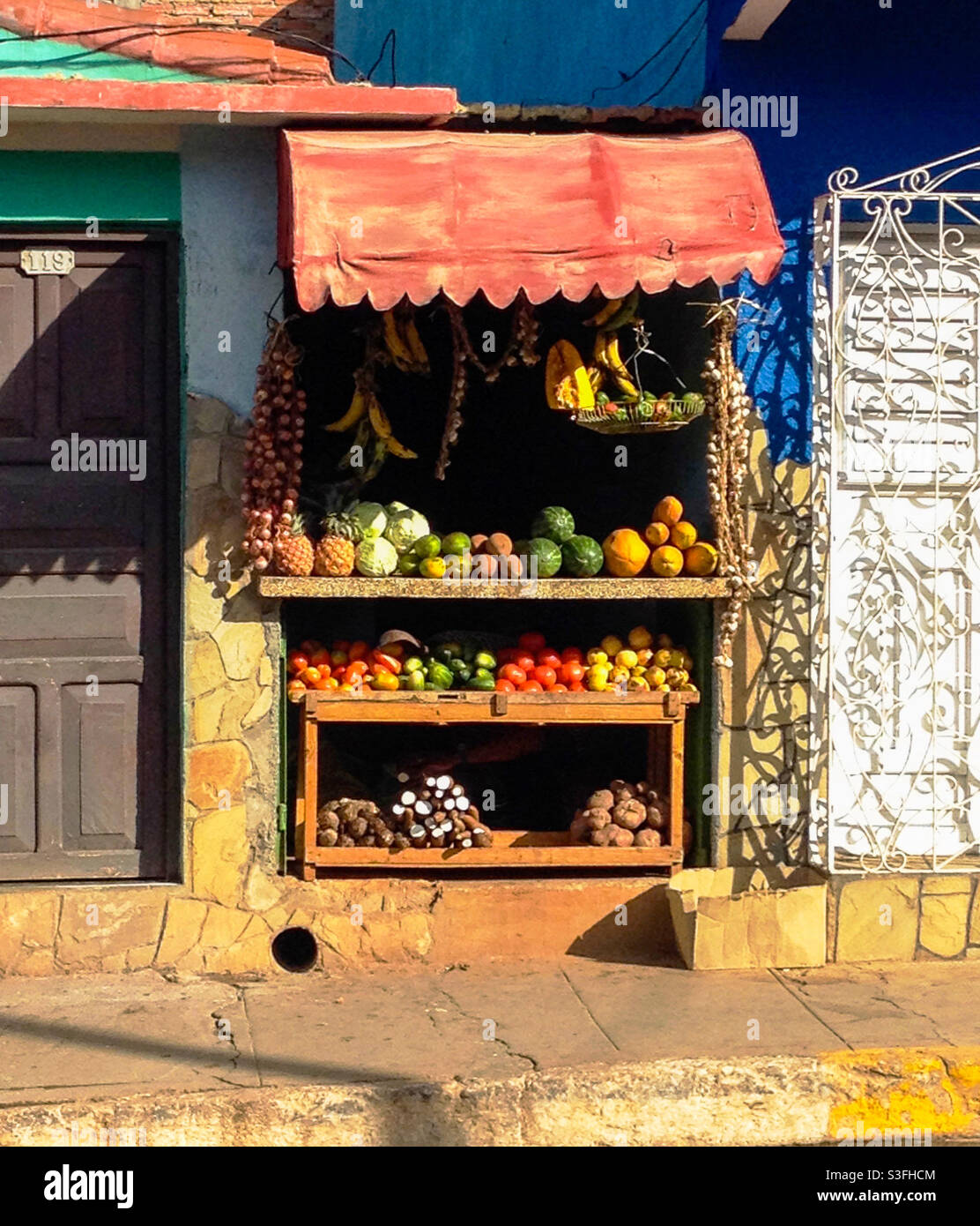 Ramshackle market stall selling fruit and vegetables sandwiched between two houses in street with colourful fruit and vegetables for sale, Baracoa, Cuba - Smartphone Captured Stock Image