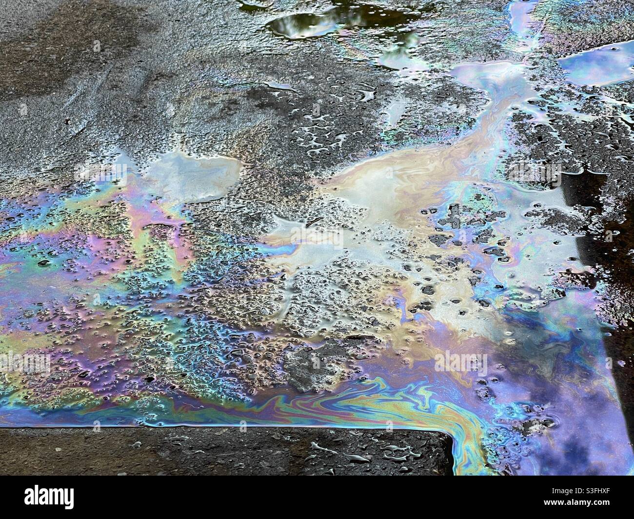 Rainbow colours from petrol spilled on the forecourt of a filling station - Smartphone Captured Stock Image