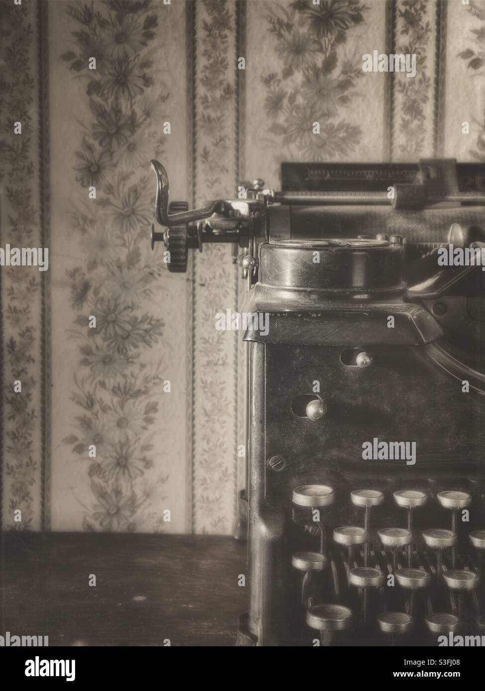 Sepia toned image of a vintage typewriter in front of vintage looking wallpaper Stock Photo