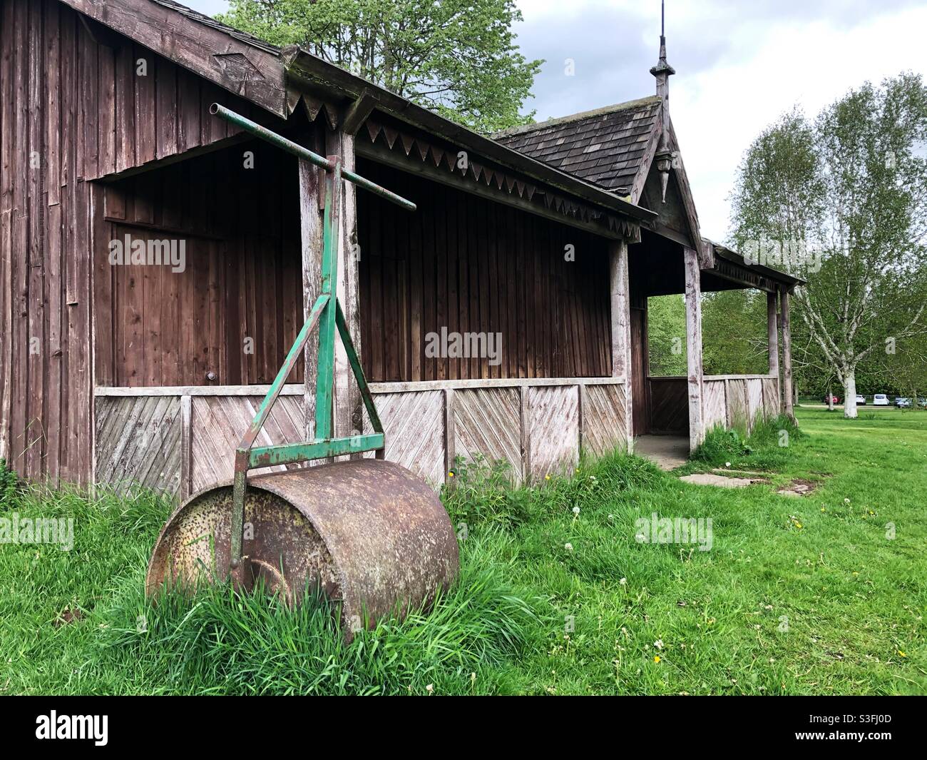 An old traditional cricket pavilion with lawn roller in a typical English countryside setting Stock Photo
