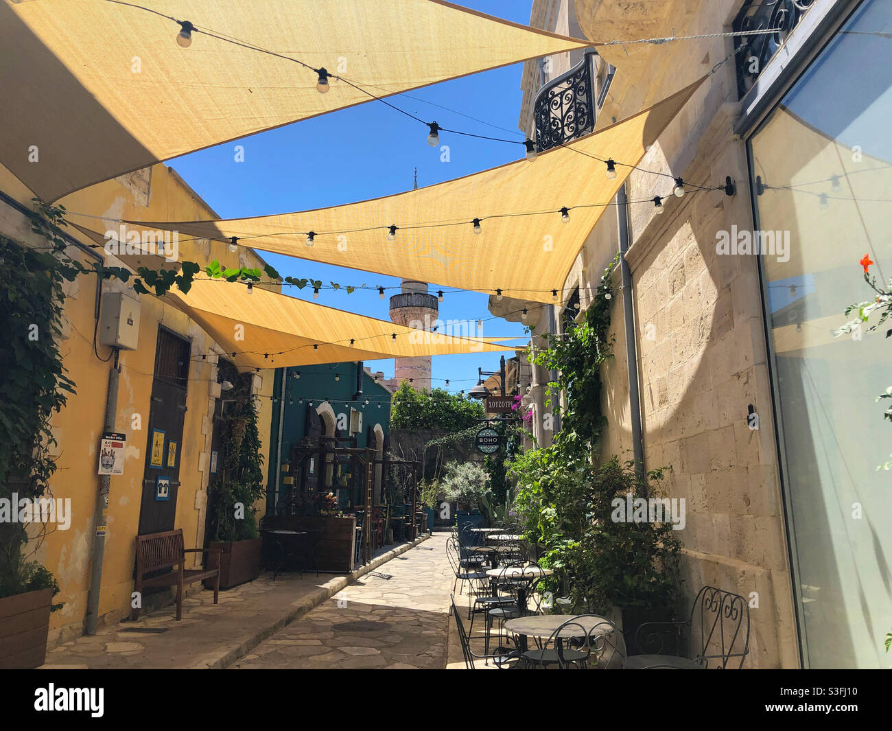 View of sidewalk cafe chairs in a narrow street in the Old Town section of Limassol, Cyprus in May 2021. At the end of the street is the Kebir Mosque. - Smartphone Captured Stock Image