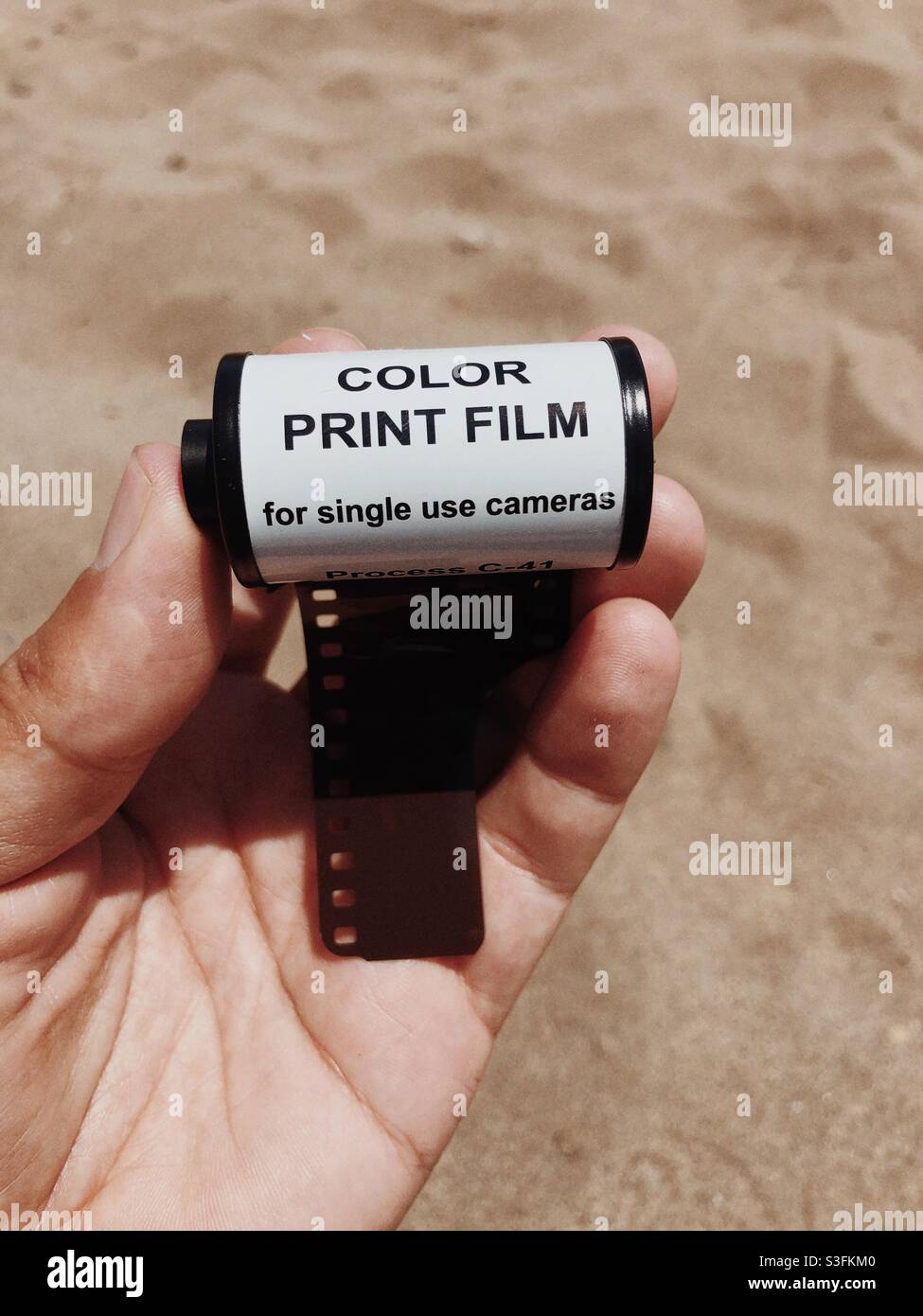 A roll of 35mm color film on hand against sandy background Stock Photo