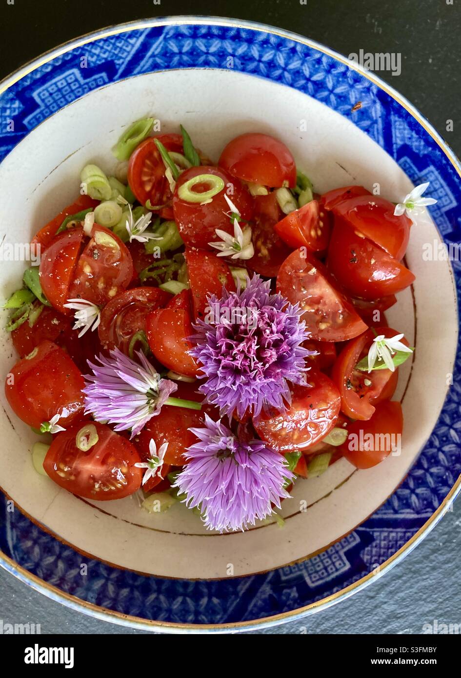 Tomato salad with garlic flowers, chive flowers and chopped spring onions in a blue and white