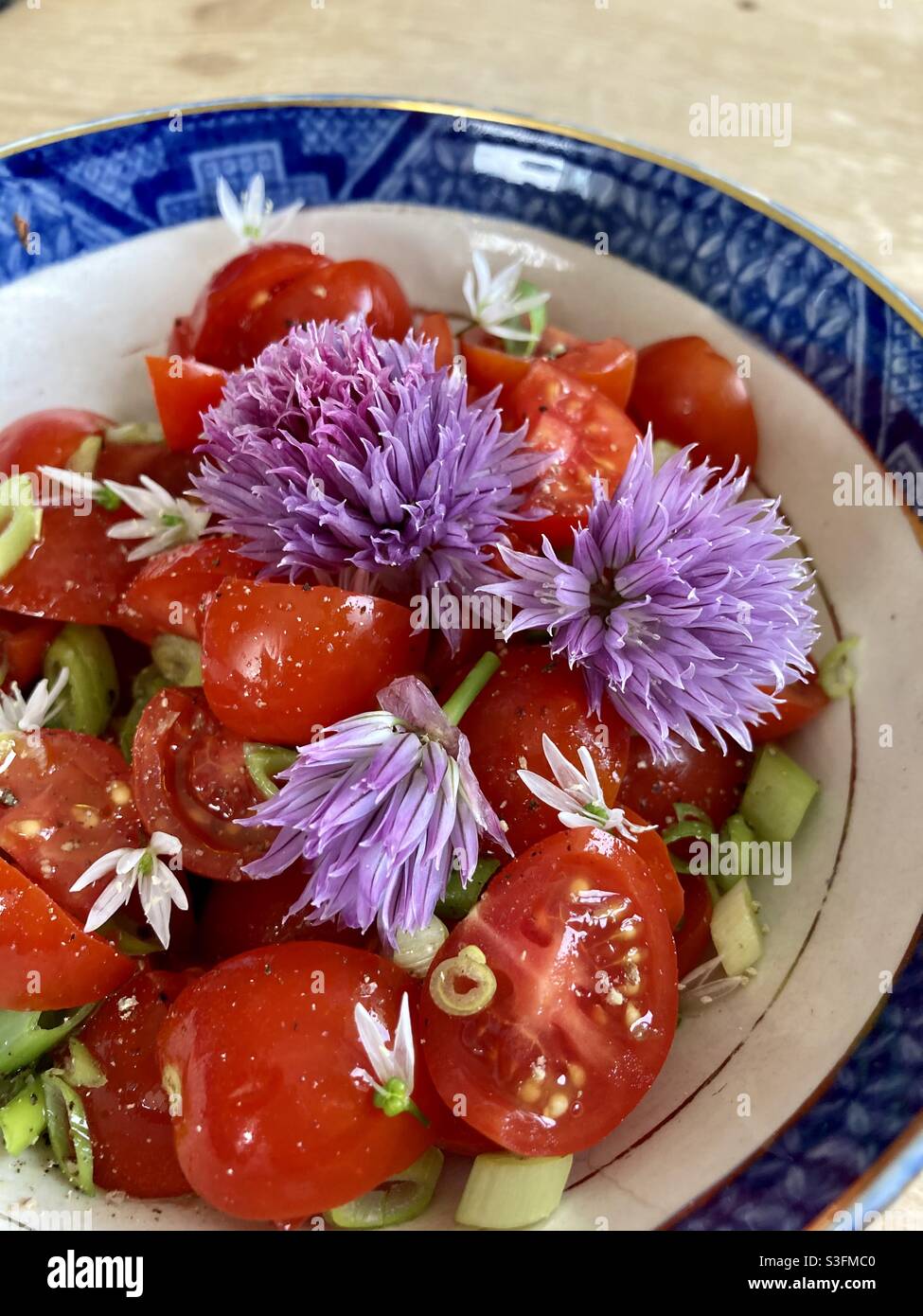 Tomato salad with purple chive flowers and sliced spring onions with wild garlic flowers - spring salad- purple and red salad - blue rim bowl Stock Photo