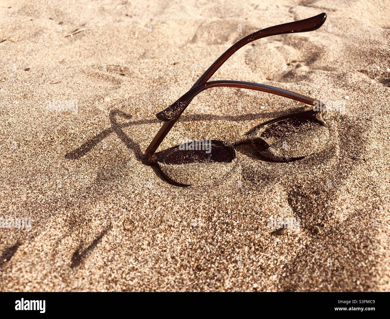 Sunglasses half buried in sand on a beach Stock Photo