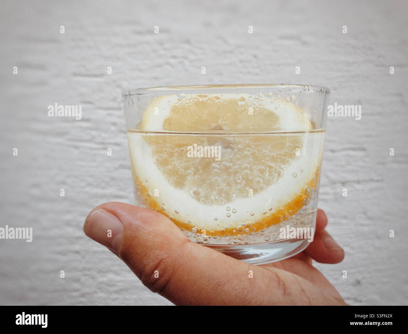 A  refreshing  drink of sparkling water serving a small glass with a big slice of lemon inside the glass - Smartphone Captured Stock Image