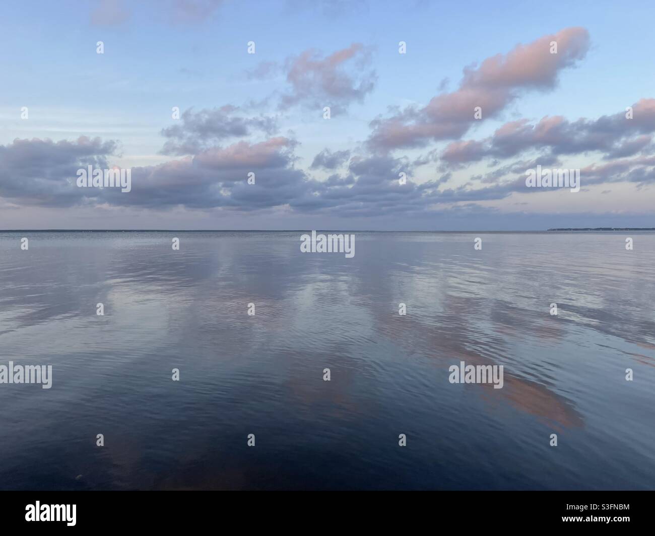 Soft evening sunset clouds and skies reflecting onto still bay water - Smartphone Captured Stock Image
