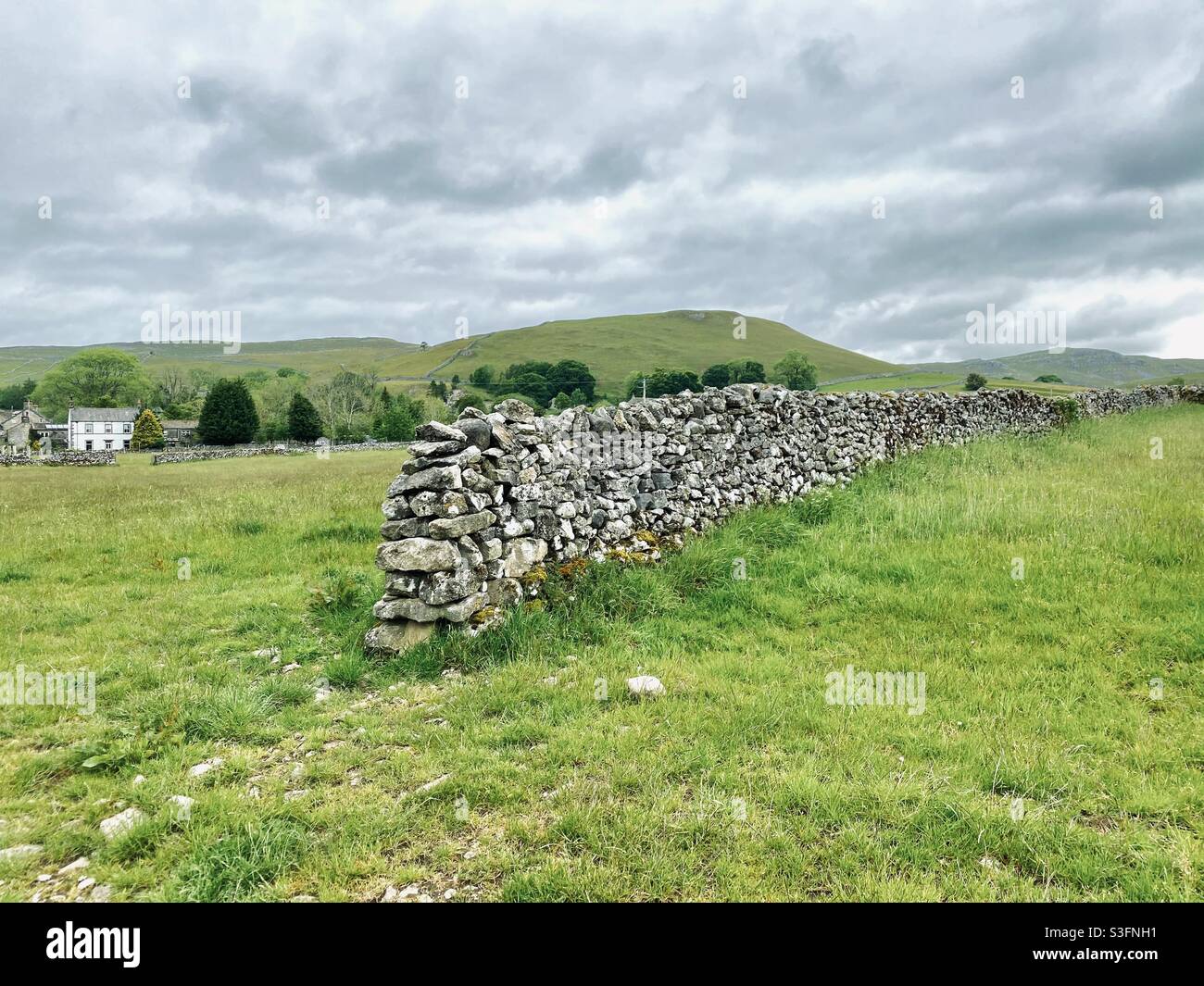 Scenic rural landscape with dramatic grey sky in Malham, Yorkshire Dales National Park, UK. Rolling hills and green pastures with dry stone wall - Smartphone Captured Stock Image