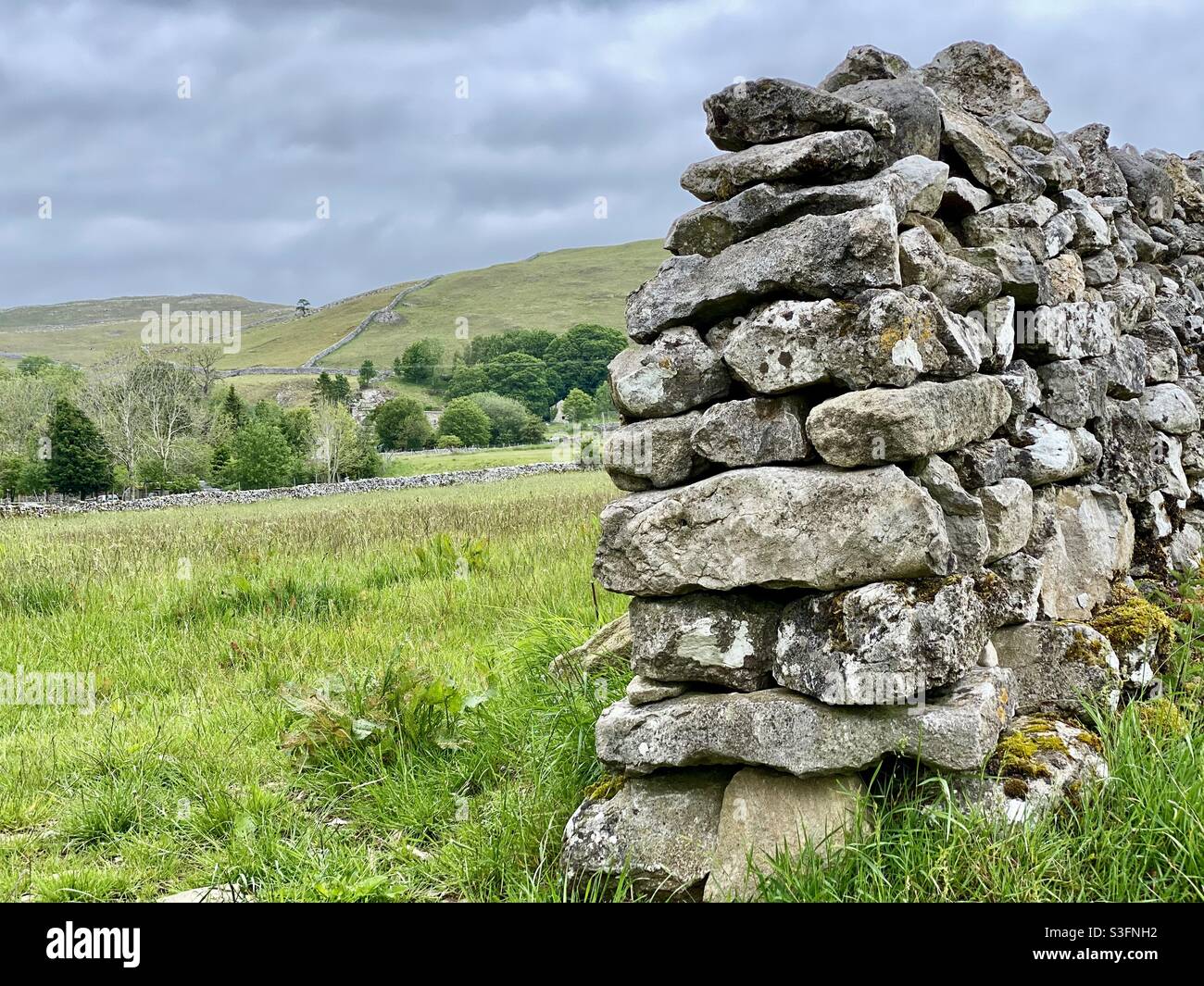 Scenic rural landscape with dramatic grey sky in Malham, Yorkshire Dales National Park, UK. Rolling hills and green pastures with dry stone wall and copy space - Smartphone Captured Stock Image