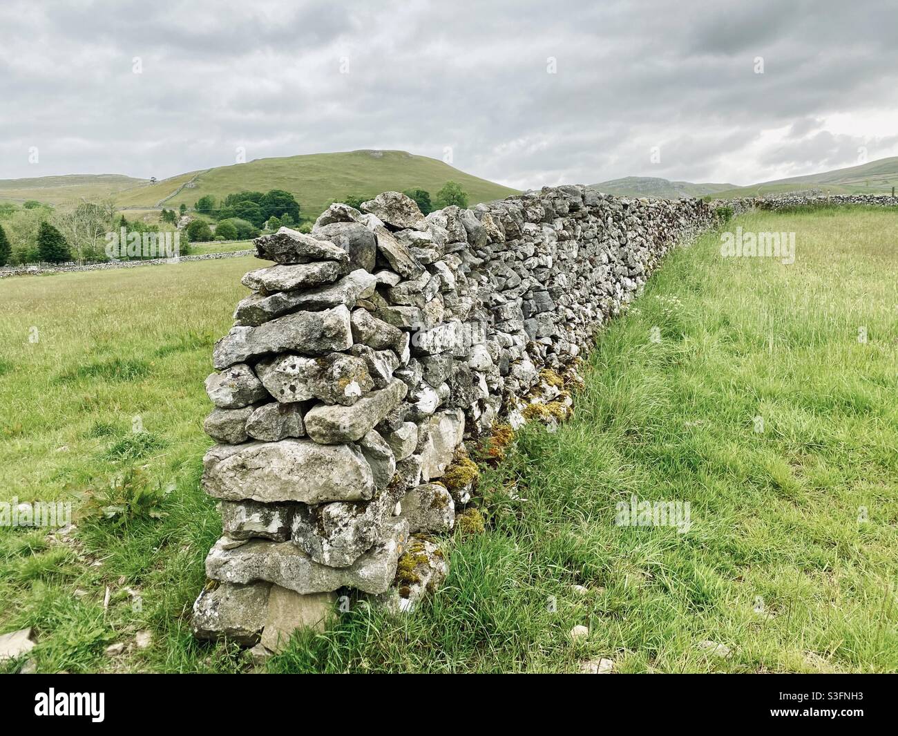 Scenic rural landscape with dramatic grey sky in Malham, Yorkshire Dales National Park, UK. Rolling hills and green pastures with dry stone walls - Smartphone Captured Stock Image