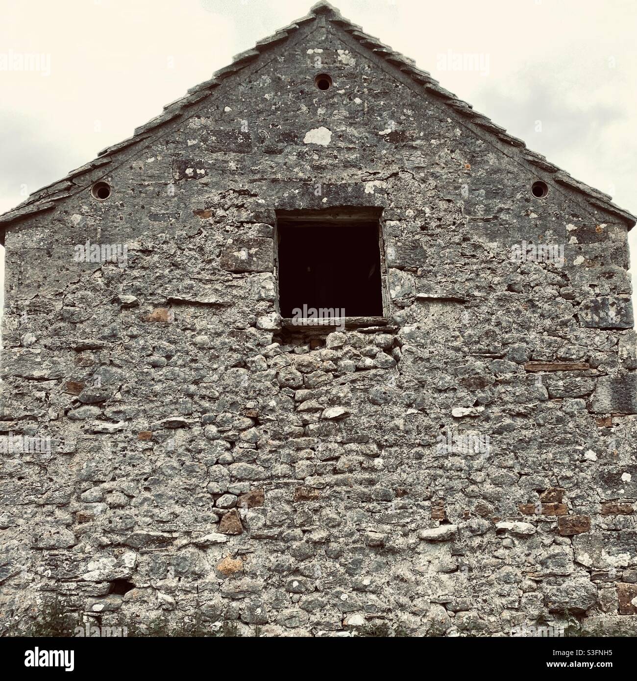 Architectural details on the gable end of an old stone farm building with window. Ancient stone barn - Smartphone Captured Stock Image