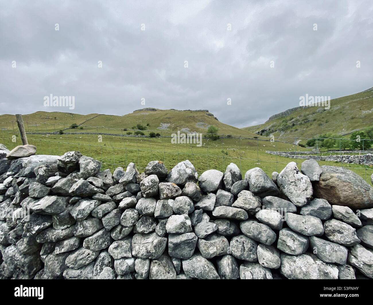 Scenic rural landscape with dramatic grey sky in Malham, Yorkshire Dales National Park, UK. Rolling hills and green pastures with dry stone walls - Smartphone Captured Stock Image