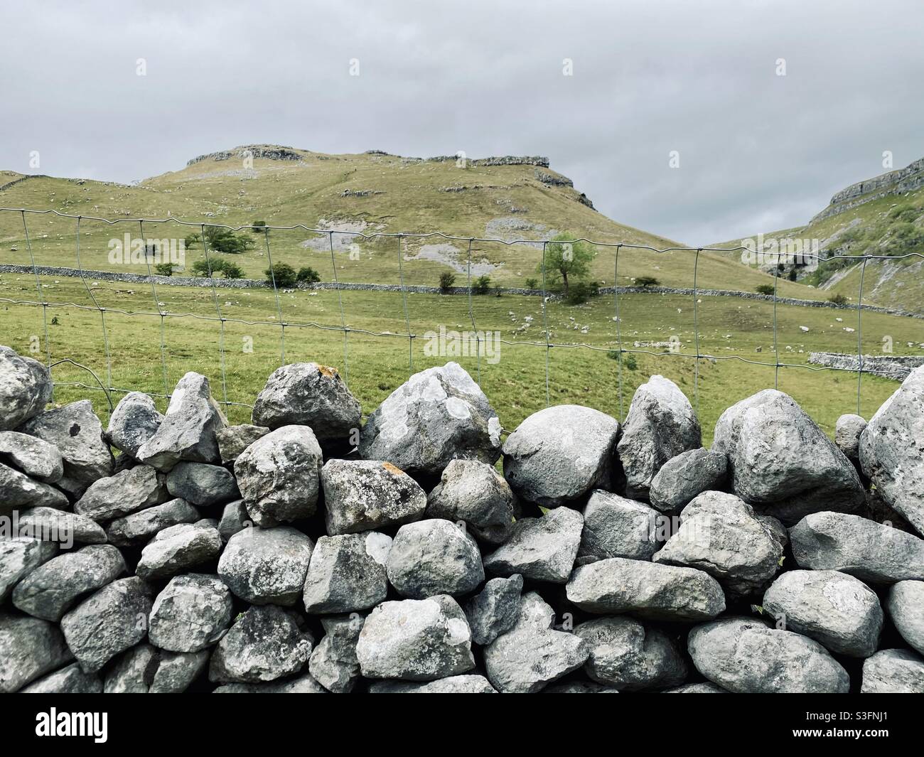 Scenic rural landscape with dramatic grey sky in Malham, Yorkshire Dales National Park, UK. Rolling hills and green pastures with dry stone walls - Smartphone Captured Stock Image