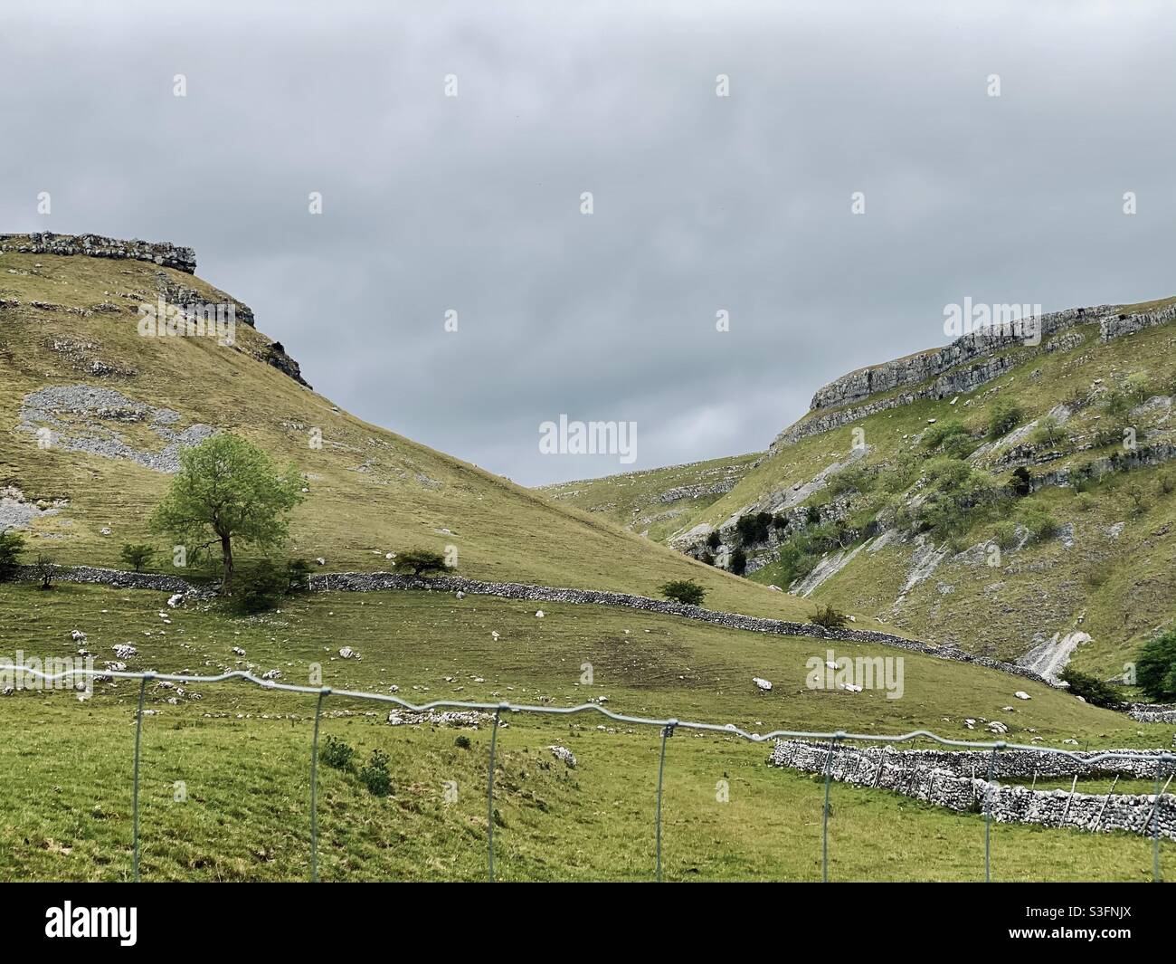 Scenic rural landscape with dramatic grey sky in Malham, Yorkshire Dales National Park, UK. Rolling hills and green pastures with dry stone walls - Smartphone Captured Stock Image