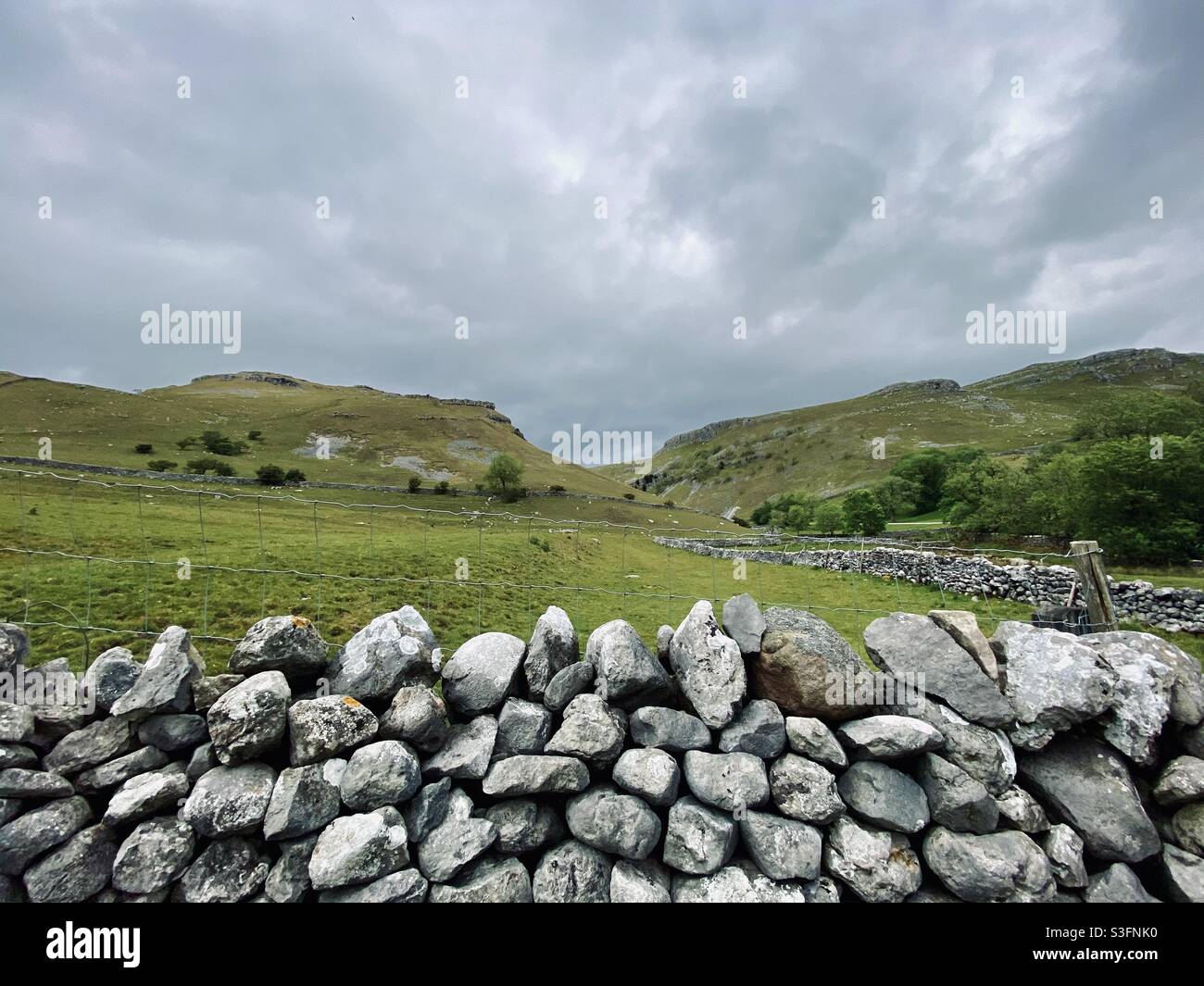 Scenic rural landscape with dramatic grey sky in Malham, Yorkshire Dales National Park, UK. Rolling hills and green pastures with dry stone walls - Smartphone Captured Stock Image