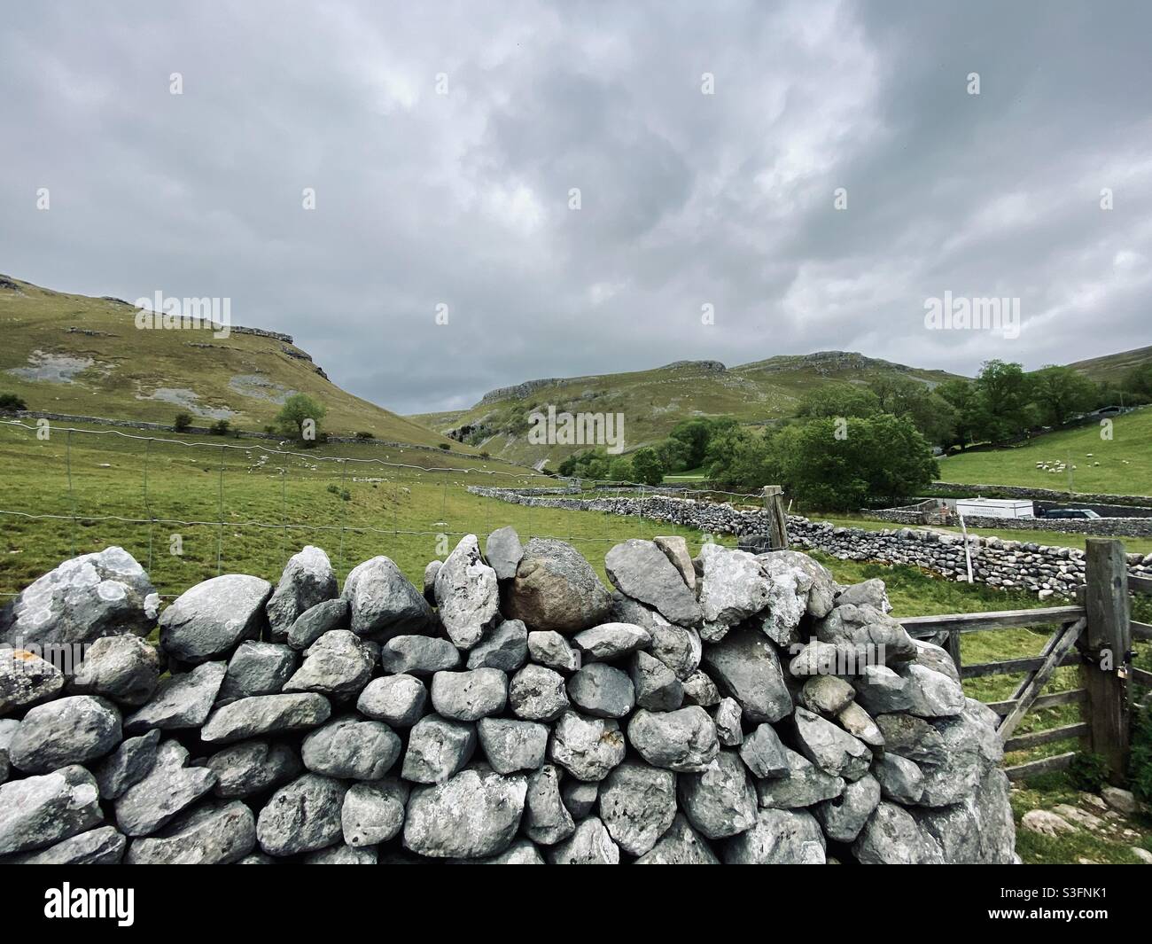 Scenic rural landscape with dramatic grey sky in Malham, Yorkshire Dales National Park, UK. Rolling hills and green pastures with dry stone walls - Smartphone Captured Stock Image