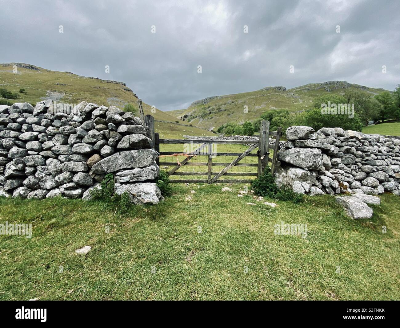 Scenic rural landscape with dramatic grey sky in Malham, Yorkshire Dales National Park, UK. Rolling hills and green pastures with dry stone walls and farm gate - Smartphone Captured Stock Image