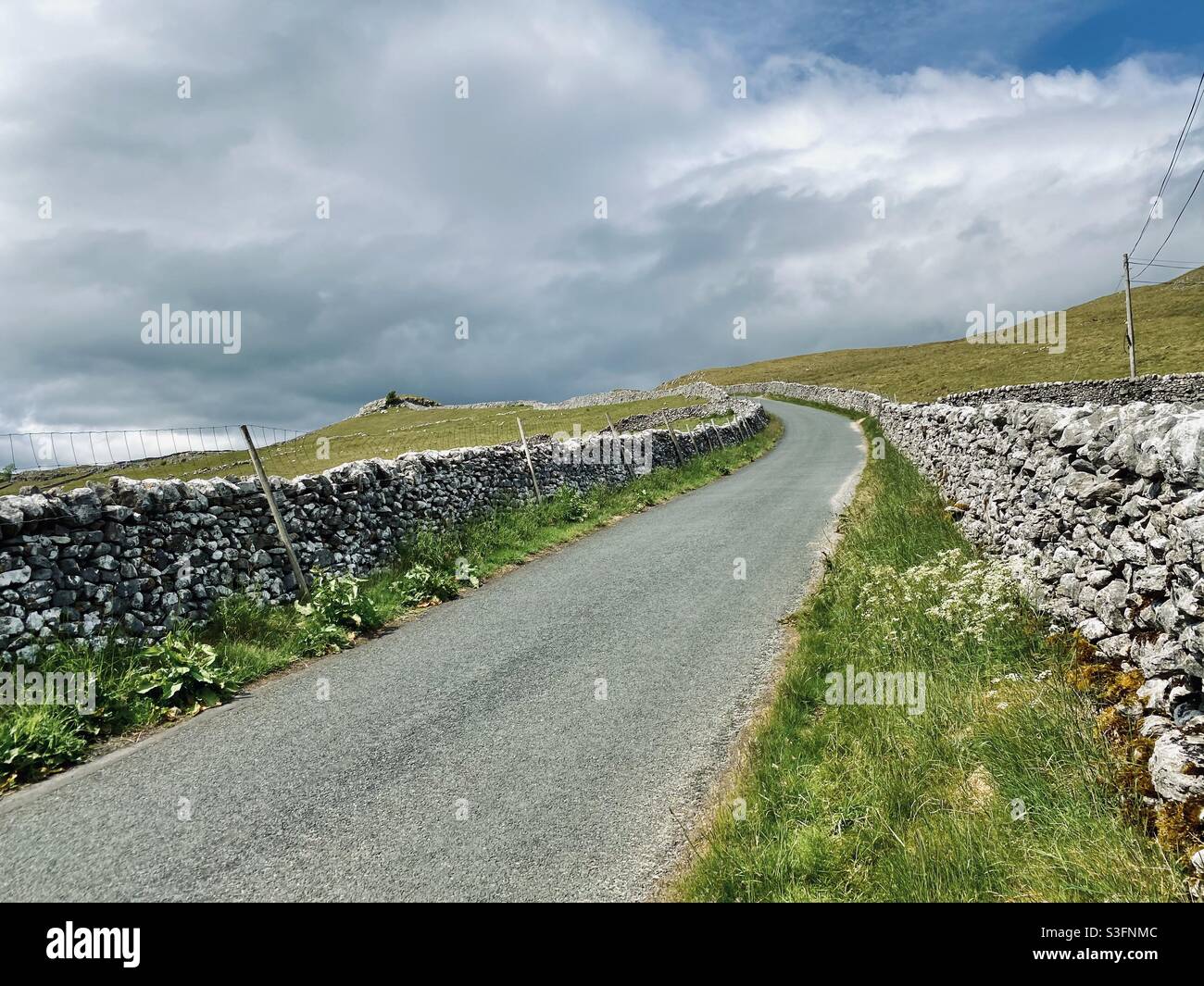 Scenic rural landscape with winding hillside road in Malham, Yorkshire Dales National Park, UK. Rolling hills and green pastures with dry stone walls. Hill walking - Smartphone Captured Stock Image