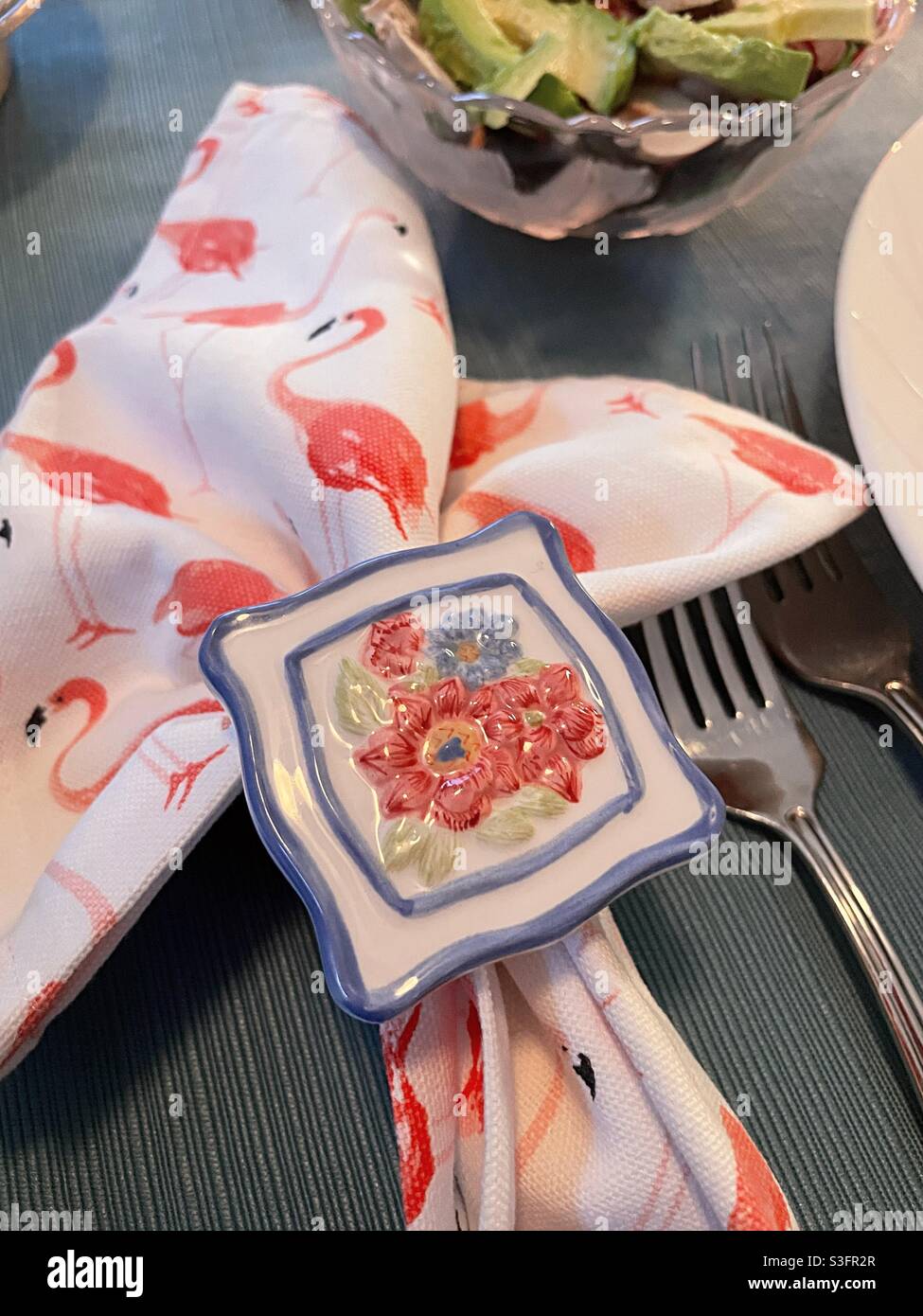 Table Setting with pink flamingo napkins being held with a brightly pattern floral napkin ring, USA - Smartphone Captured Stock Image