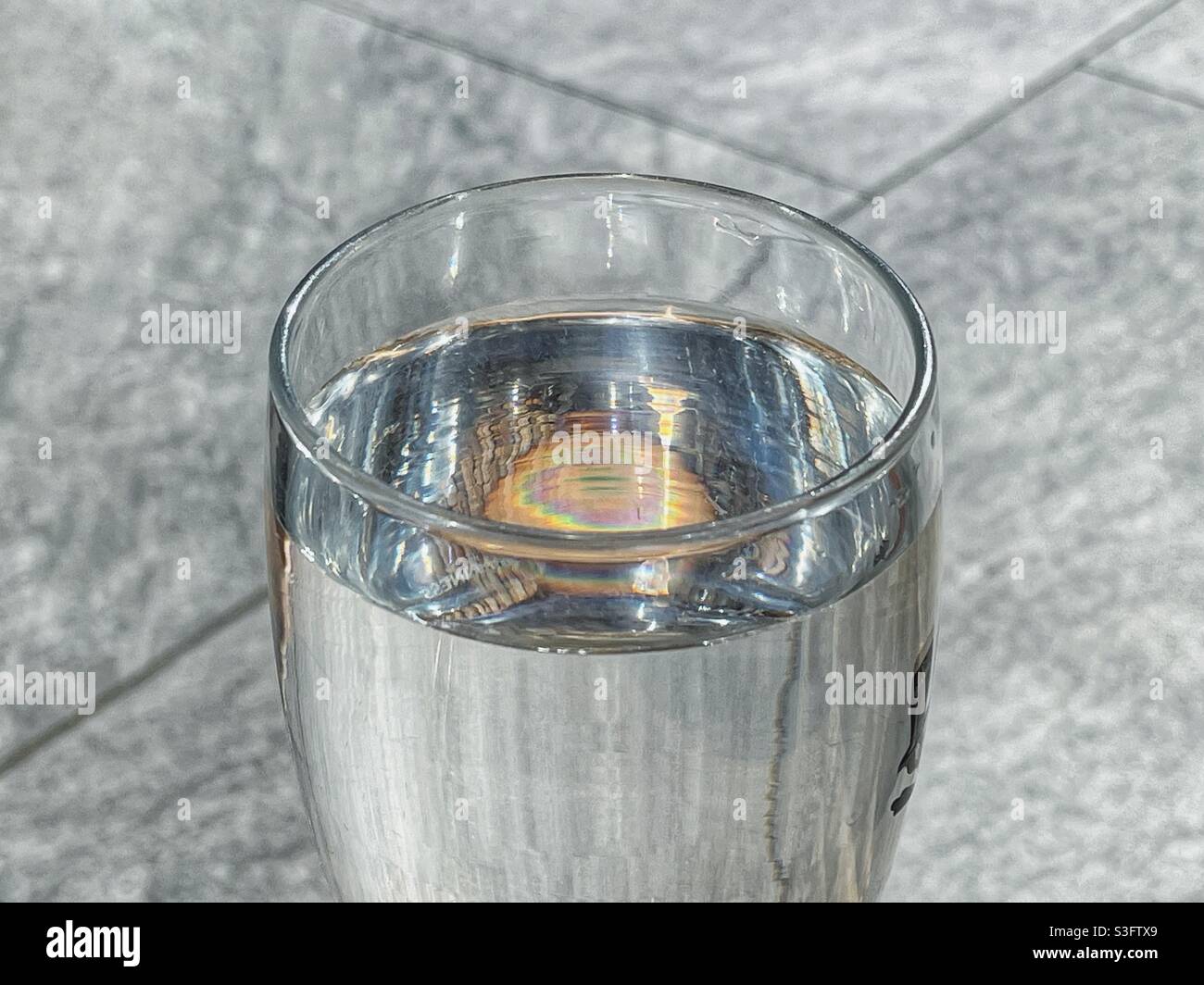 Pint glass of water backlit by sunlight against the plain background of a garden patio Stock Photo