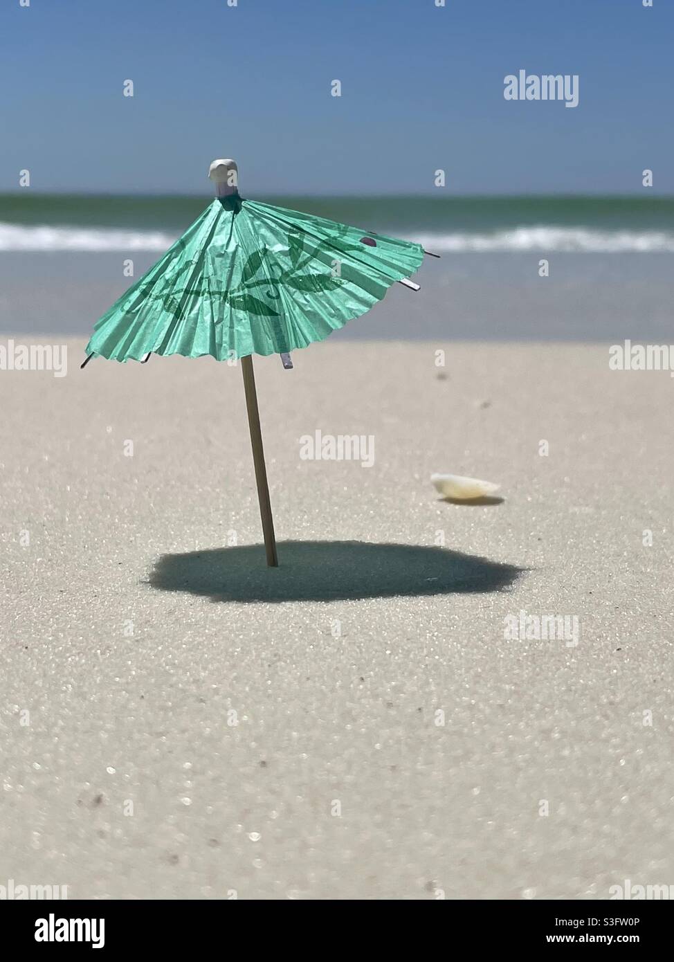 Select focus on a miniature umbrella on beach sand Stock Photo